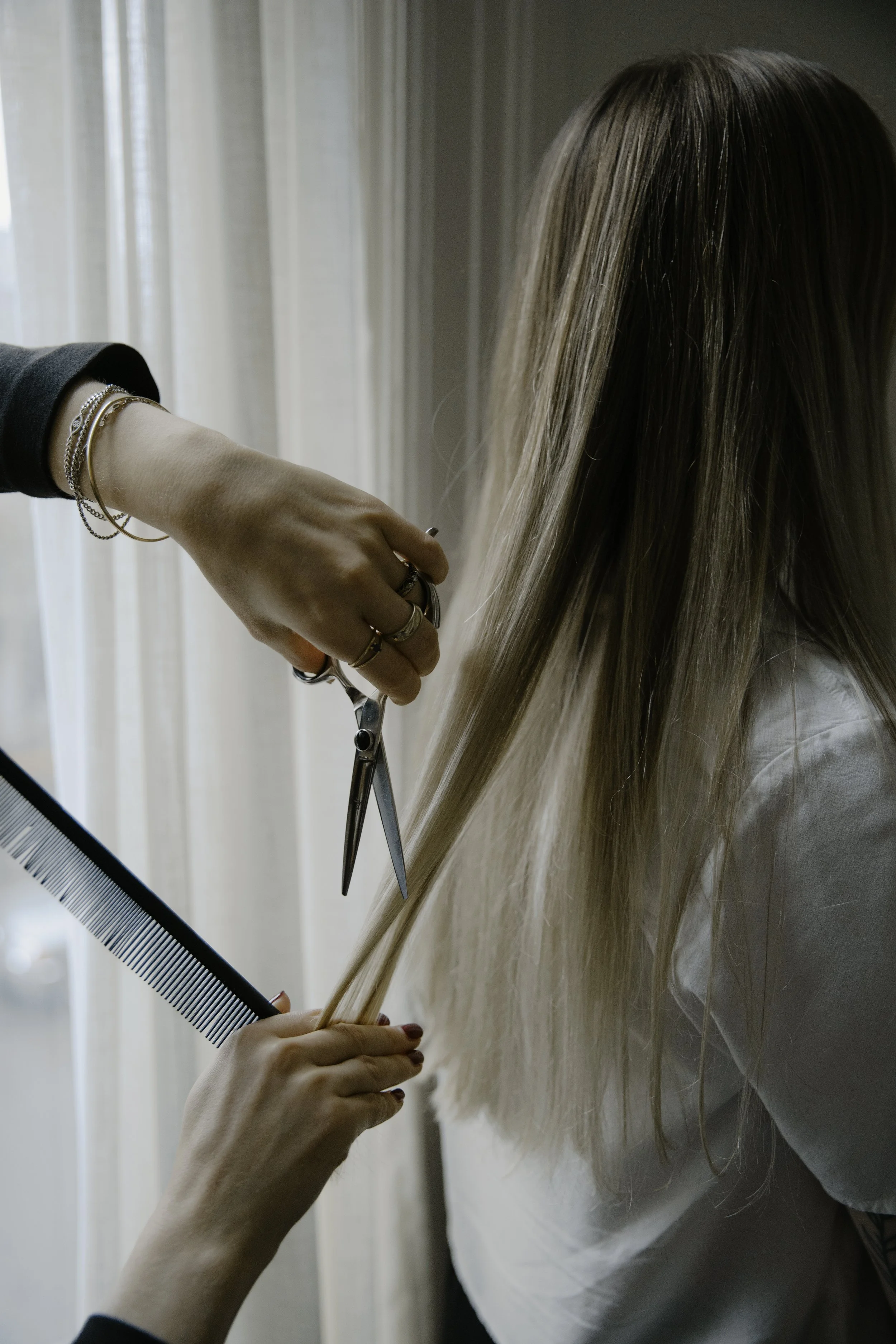 A person is having their hair cut by a hairstylist using scissors, with a comb held in the stylist's other hand.