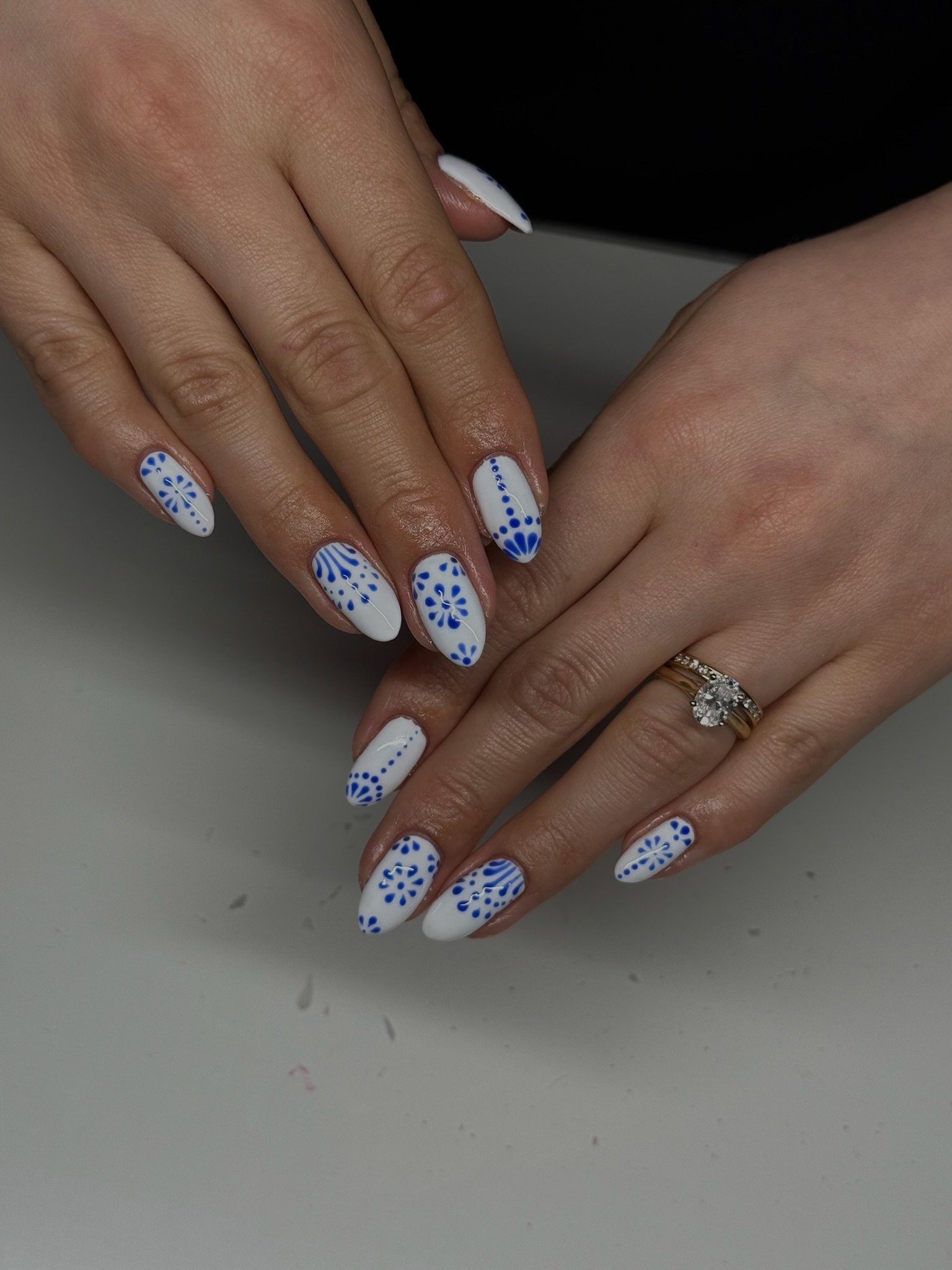 Woman's hands with white and blue floral and dotted nail art, one hand showing a ring with a big central diamond