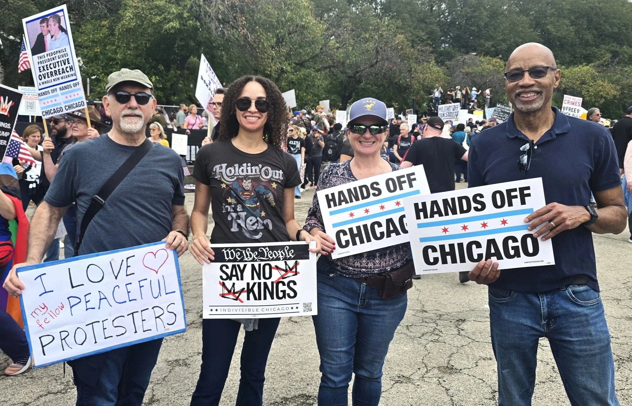 Four Indivisible Chicago protestors hold rally signs at No Kings on October 18, 2025 that say I Love Peaceful Protestors, We The People Say No Kings, and Hands Off Chicago.