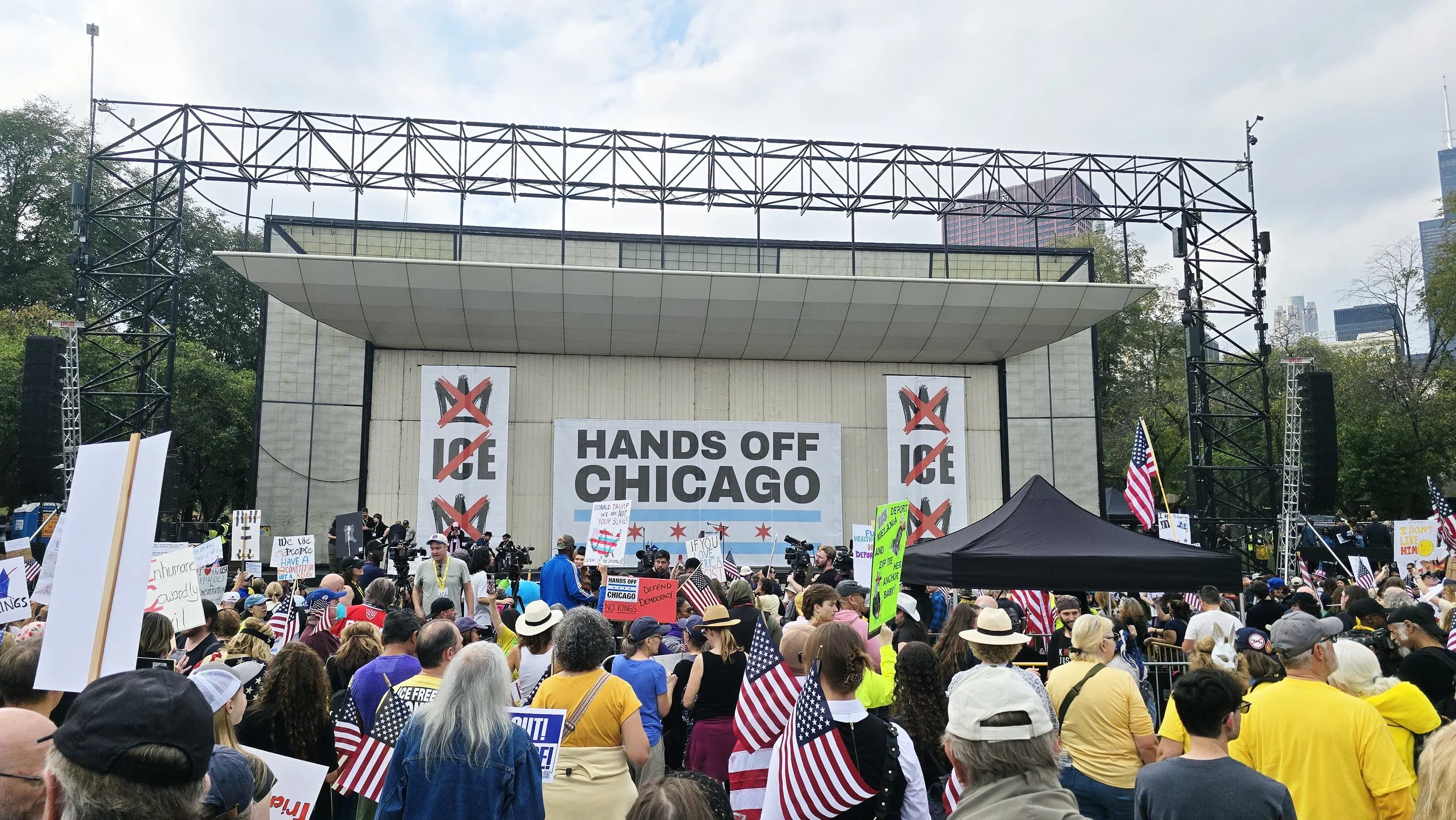 View of the crowd and stage at the Hands Off Chicago-No Kings rally and march on October 18, 2025. Large banners say Hands Off Chicago, No ICE and No Kings.