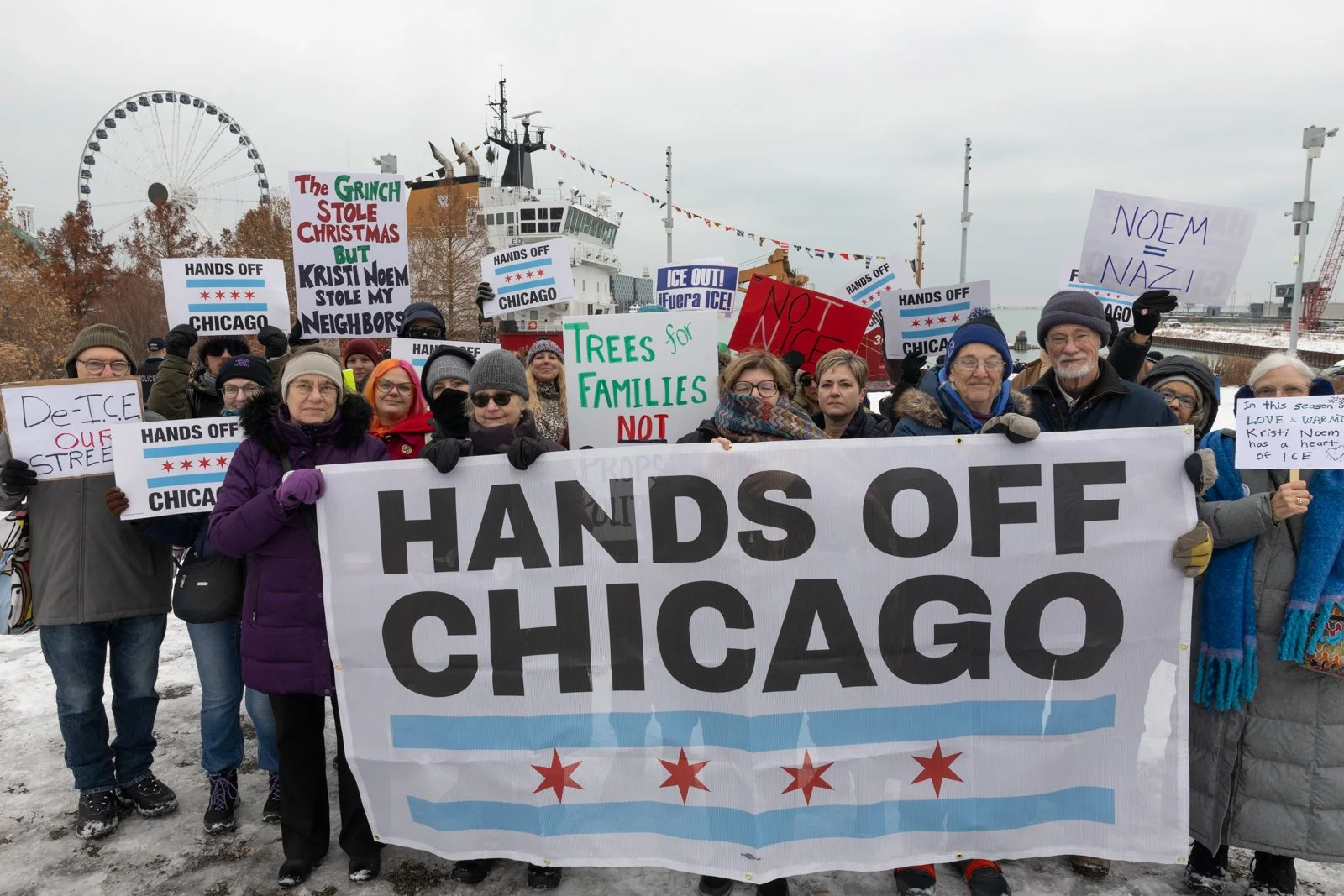 A group of Indivisible Chicago protestors hold a Hands Off Chicago banner and other signs when former DHS Secretary Kristi Noem visited Navy Pier in Chicago for a Christmas tree distribution event.