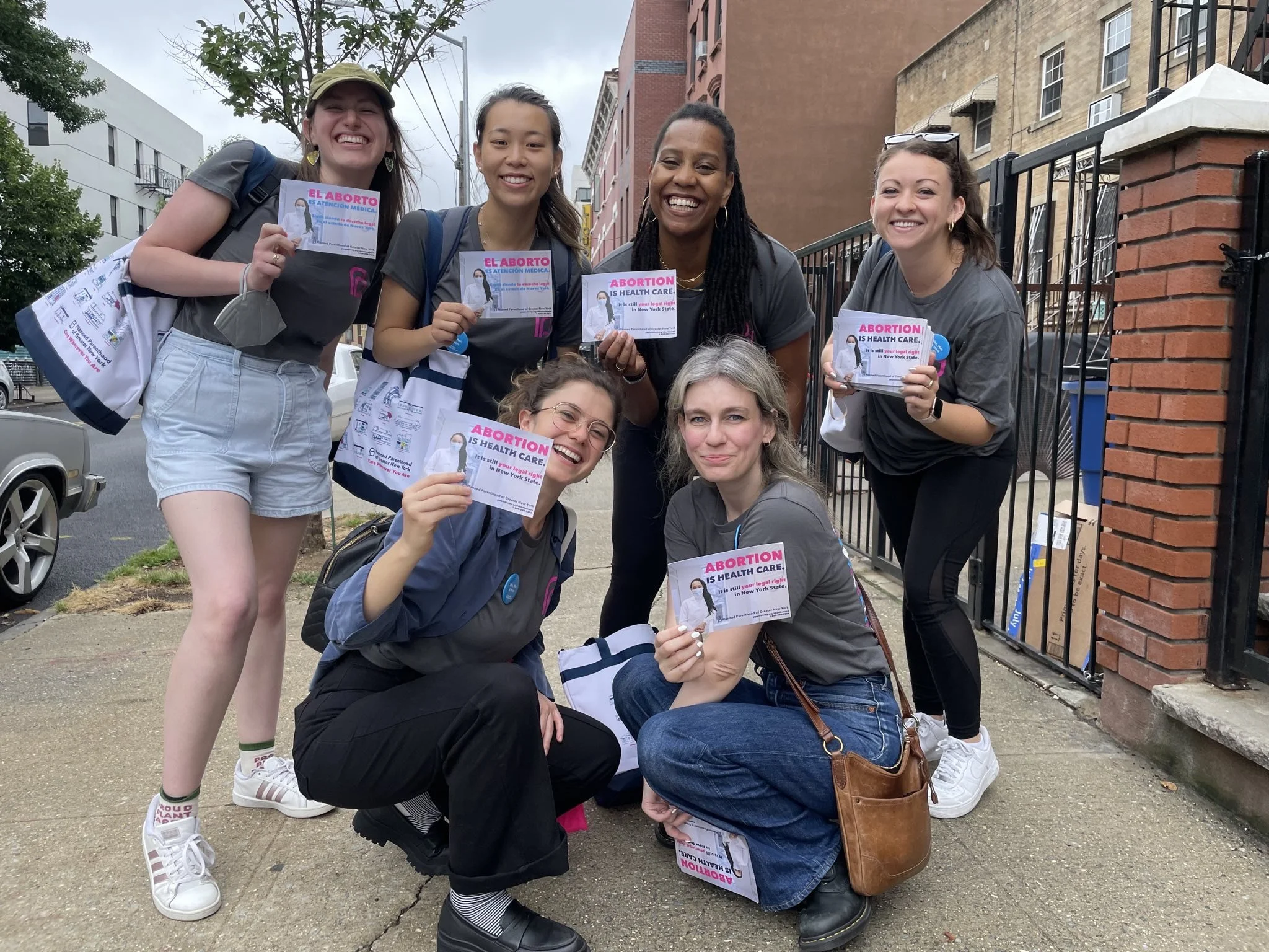A group of people outdoors holding flyers with "Abortion is Health Care" message, posing for a photo.