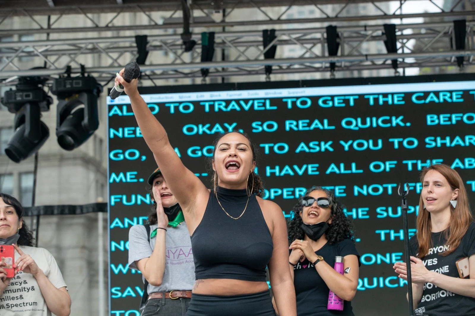 Speaker on stage holding a microphone in the air.