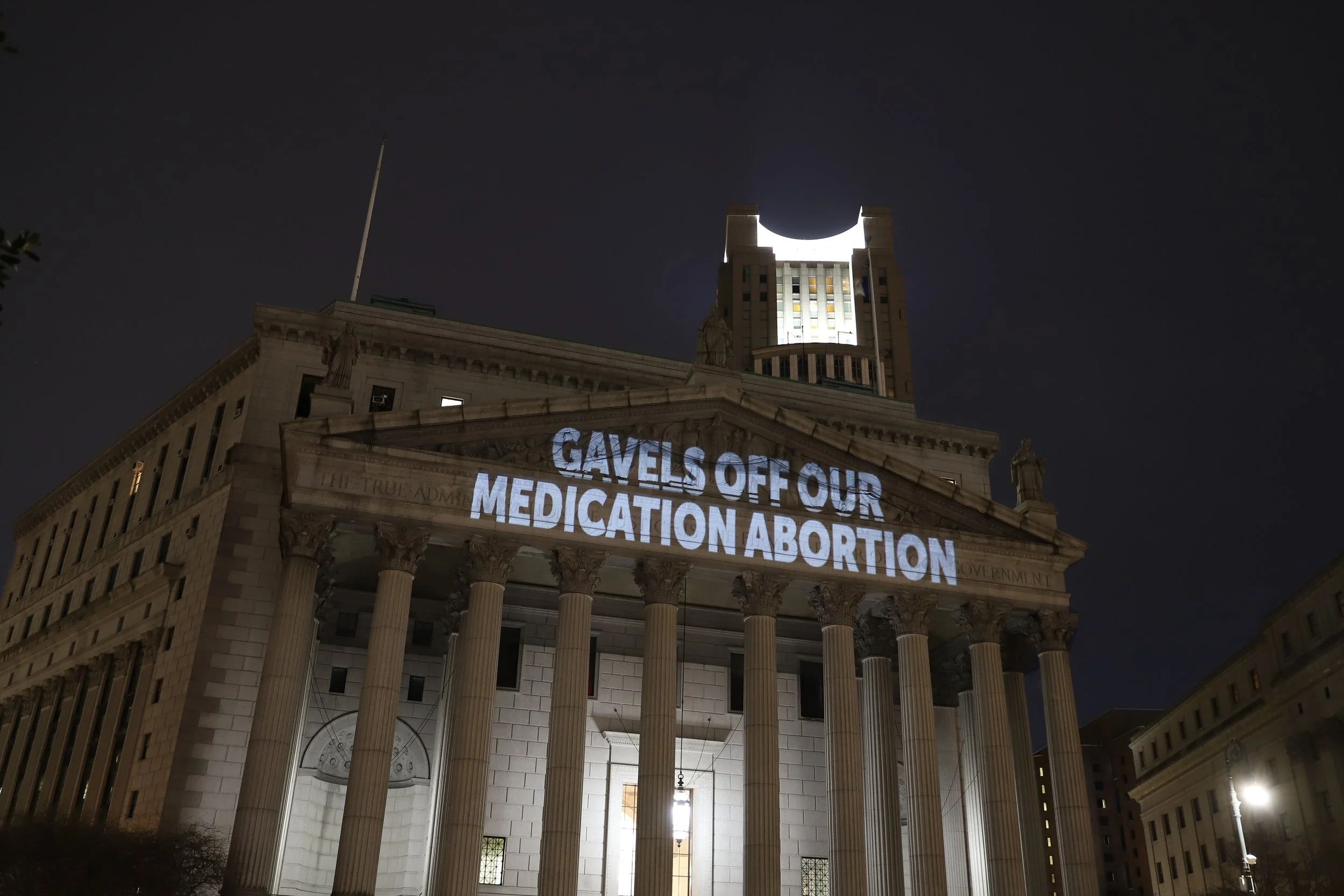 A government building at night with "Gavels Off Our Medication Abortion" projected onto it.