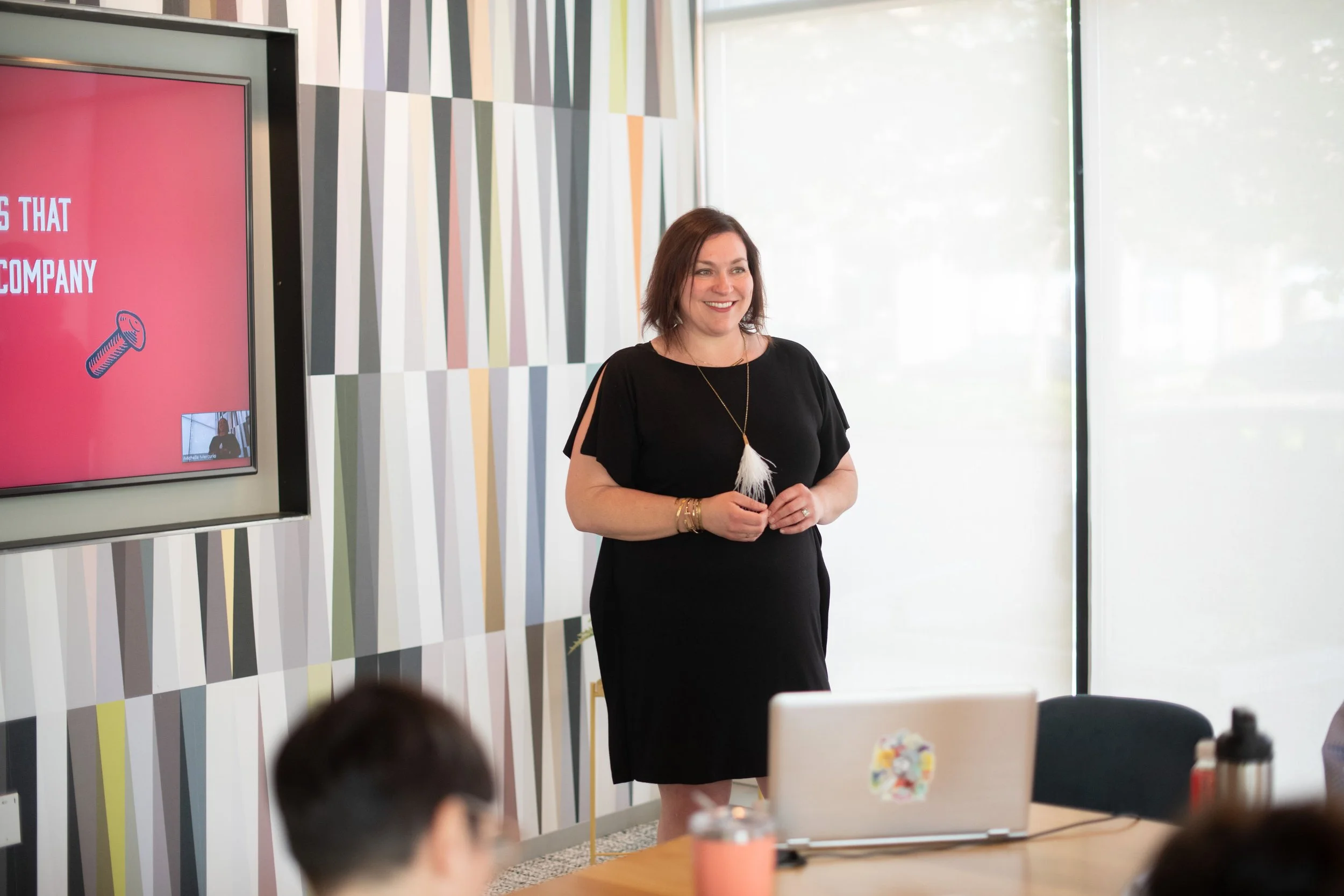 Michelle is standing in front of a conference room facilitating a session.