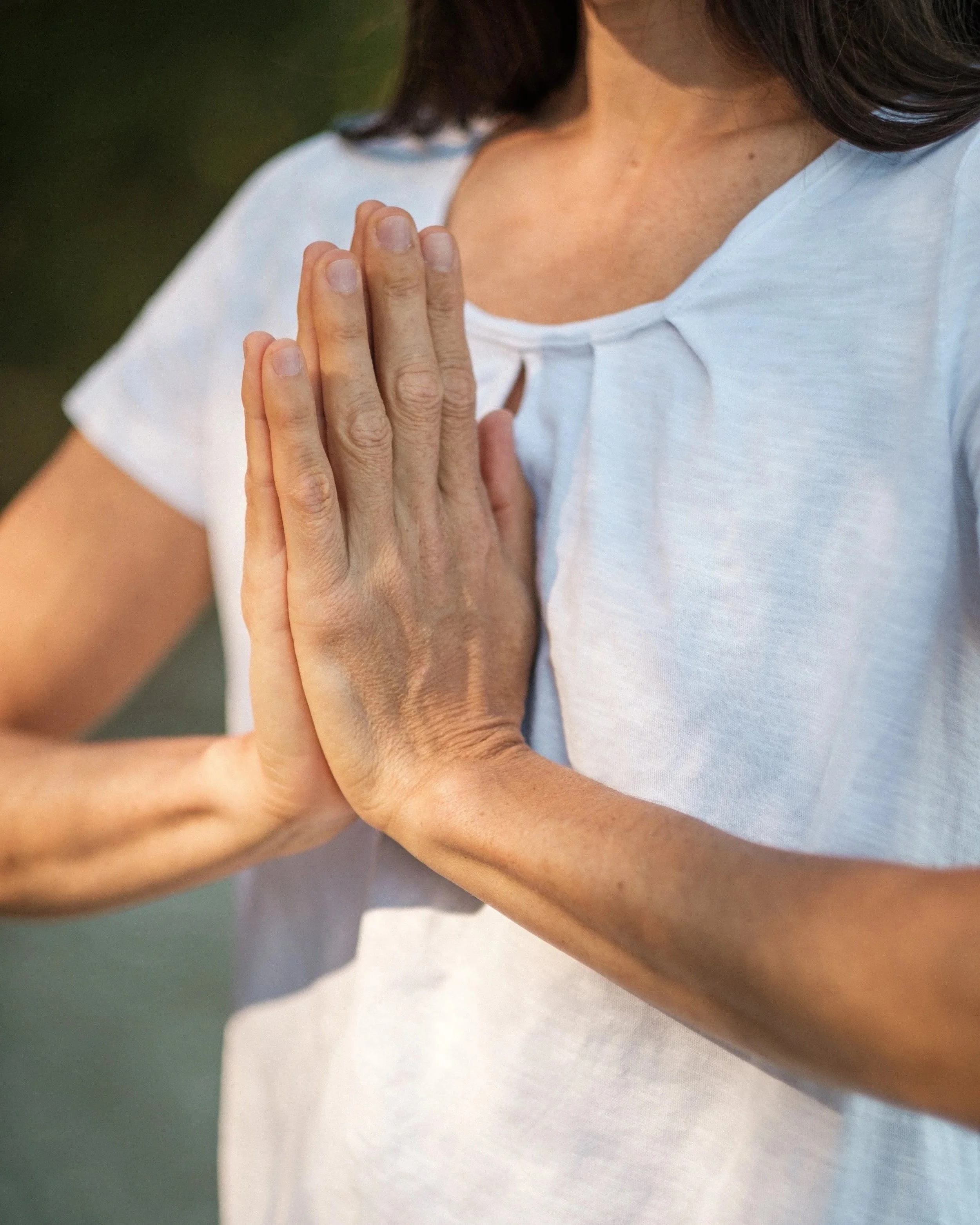 Close-up of a woman in a white shirt practicing yoga or meditation with her hands pressed together in a prayer position.