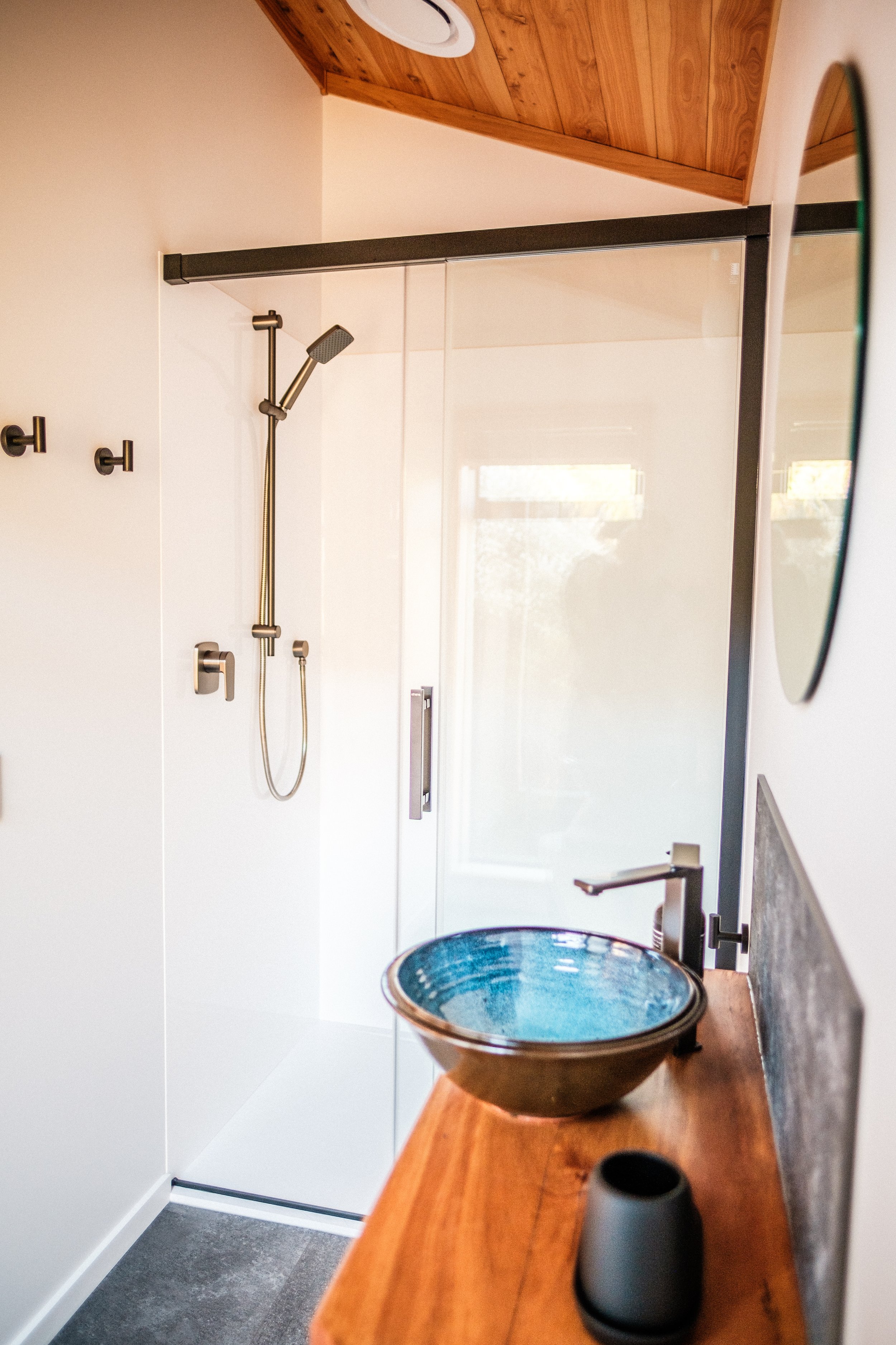 Modern bathroom with a walk-in glass shower, wooden ceiling, and a wooden countertop with a blue ceramic basin and a black faucet.