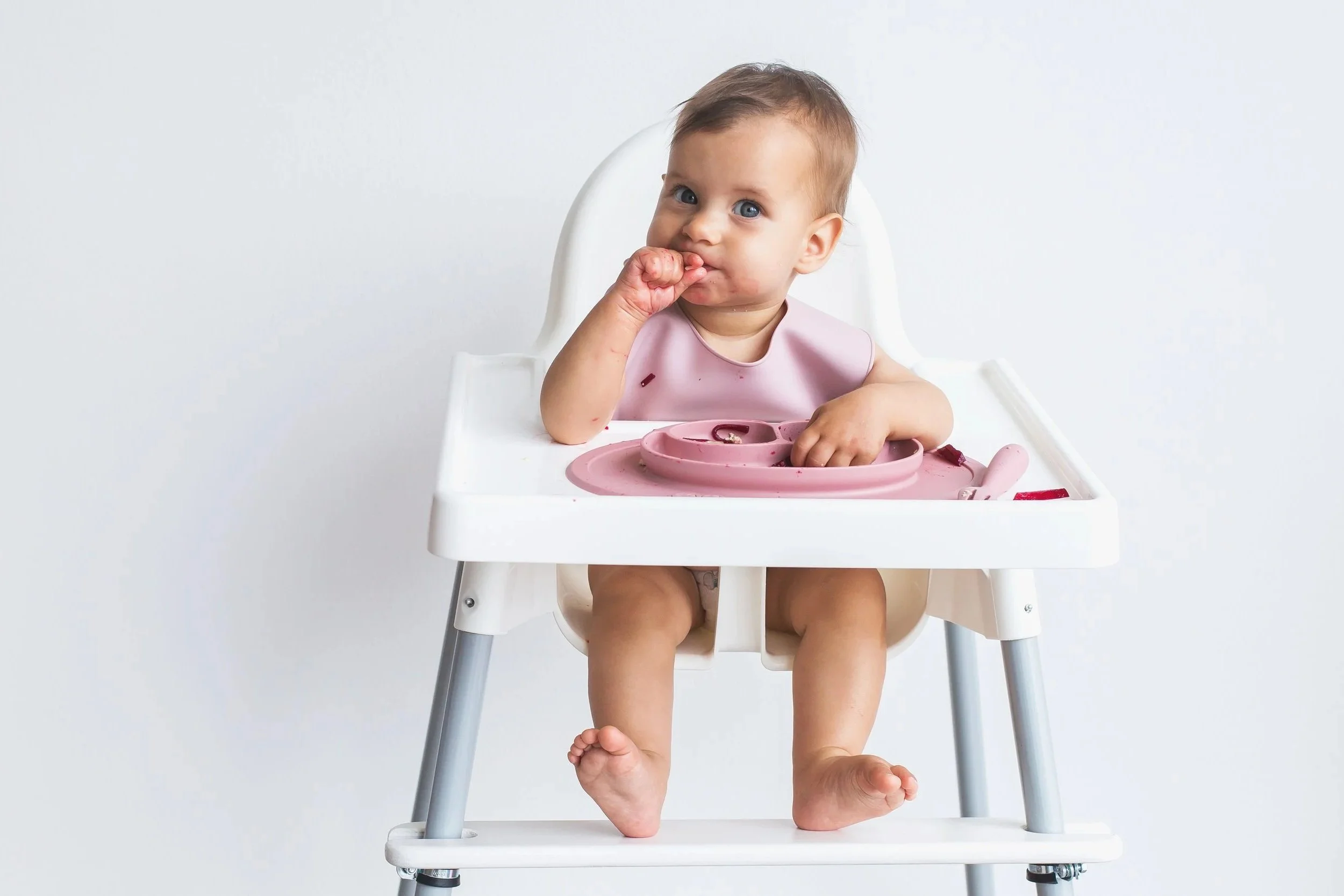 baby in high chair with a pink bib working on transitioning to solids