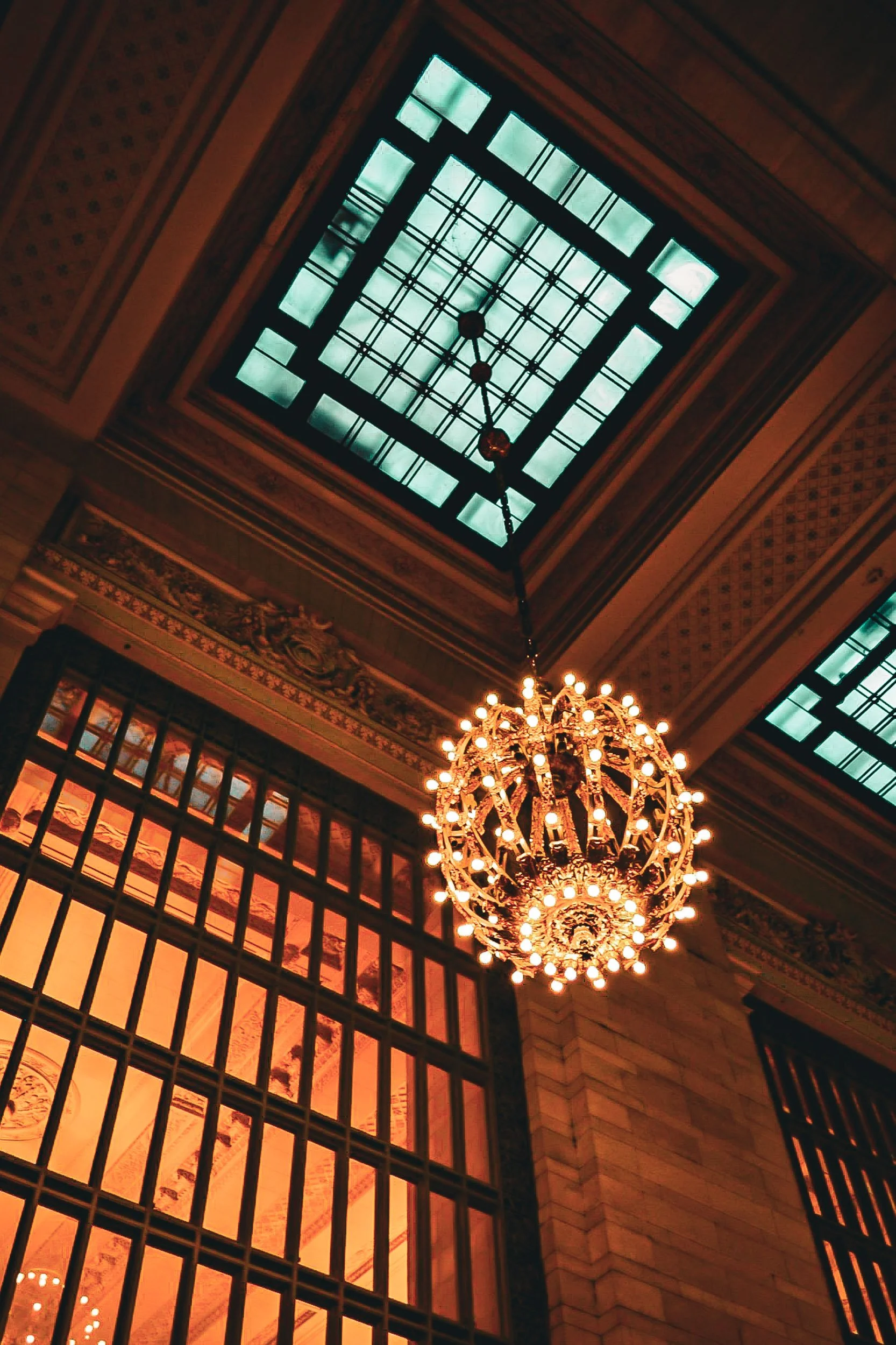 Grand Central Terminal Chandelier - A majestic vertical shot highlighting the ornate, glowing details of a historic gold chandelier suspended from the ceiling of Grand Central Terminal.