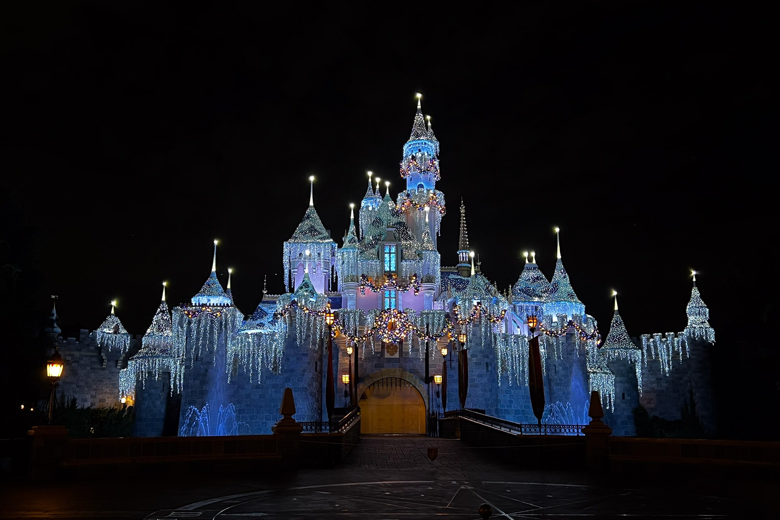 Midnight Magic - A dramatic nighttime landscape of an illuminated castle blanketed in thousands of shimmering white holiday icicle lights, casting a brilliant glow against a stark black sky.