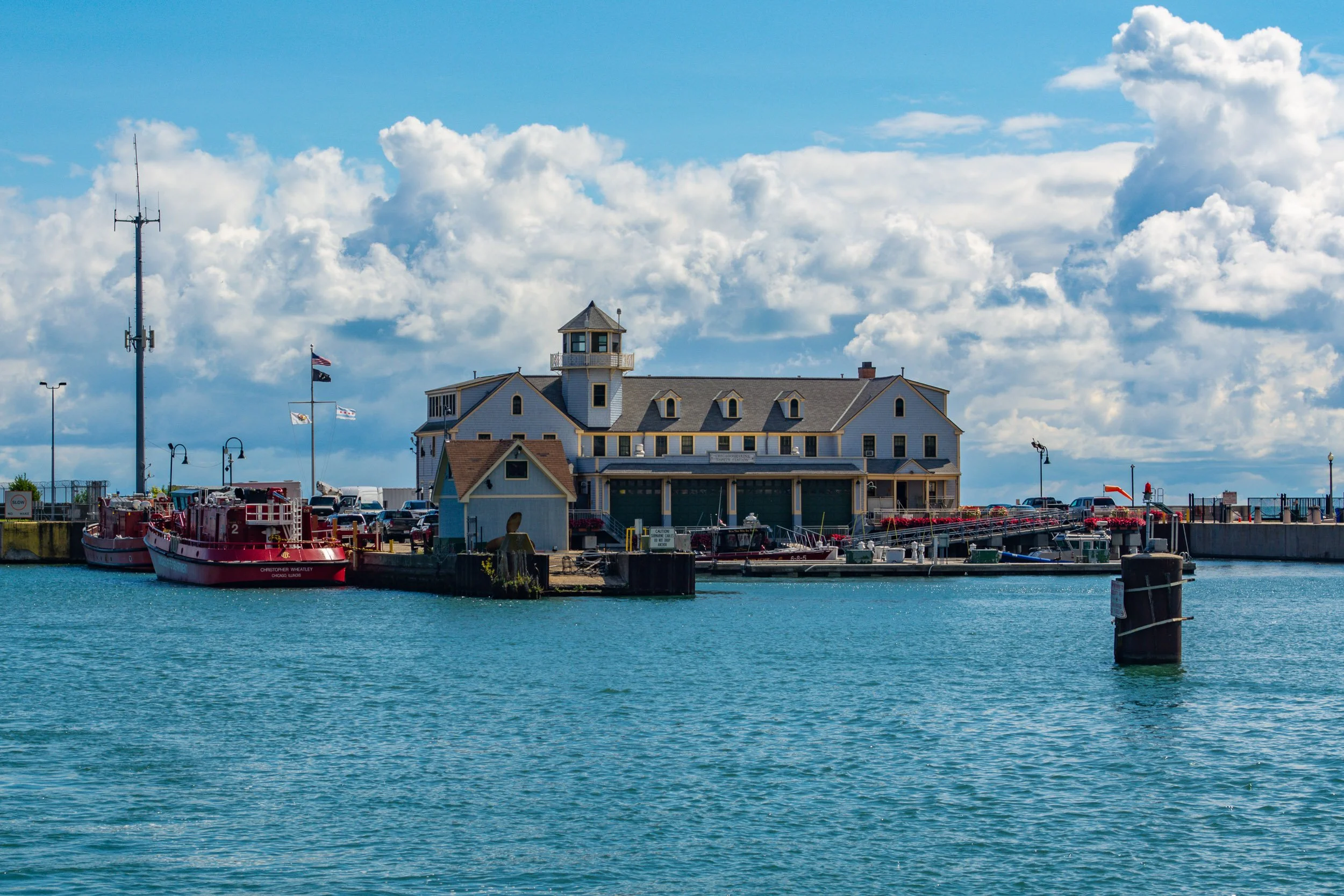 The Engine House - A wide maritime landscape featuring the Chicago Fire Department Marine Unit station near Navy Pier, flanked by red fireboats under a dramatic, cloudy blue sky.