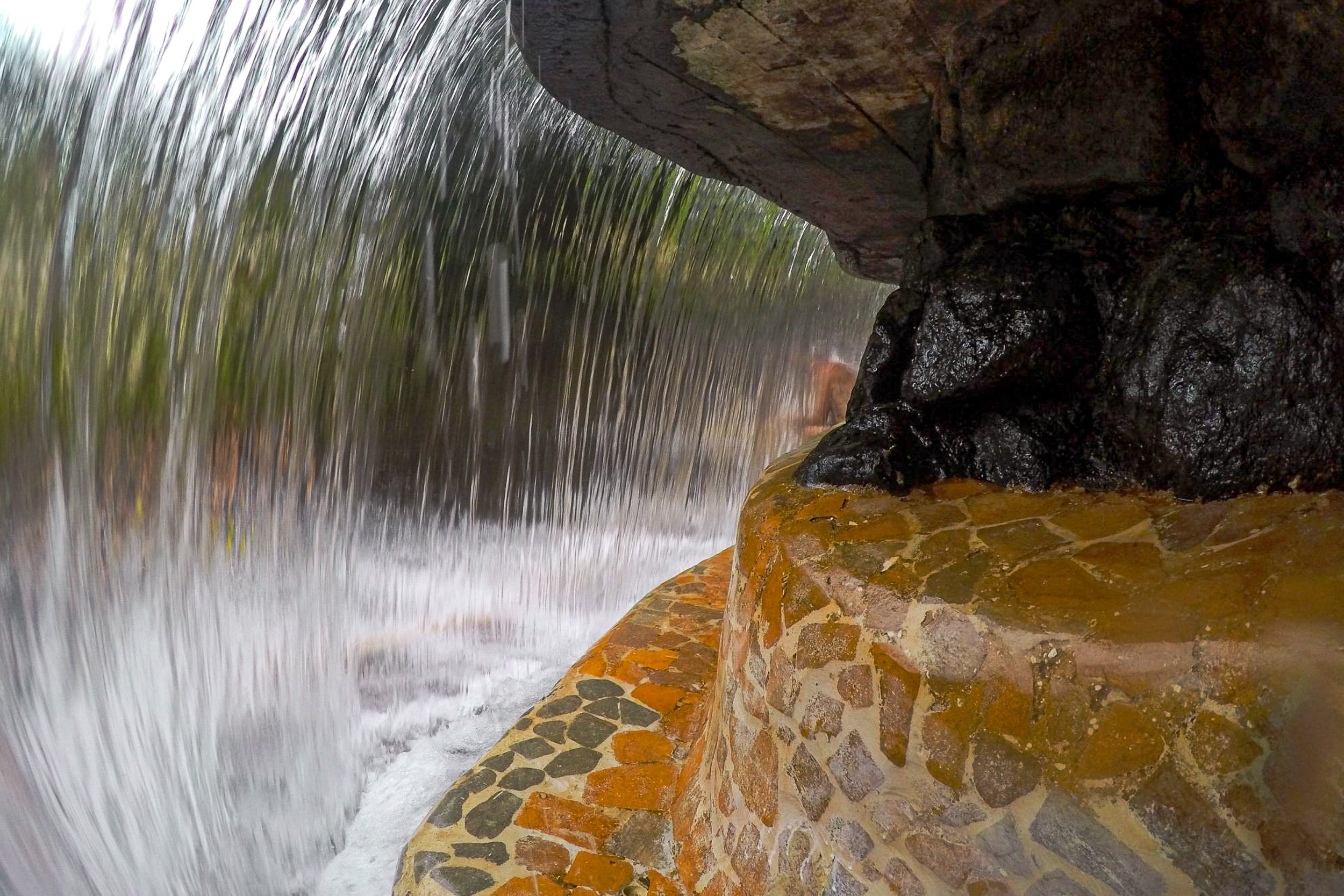 Curtain of Water - A dramatic, wide-angle perspective from behind a rushing waterfall, framing wet stone textures and a cascade of motion blur.