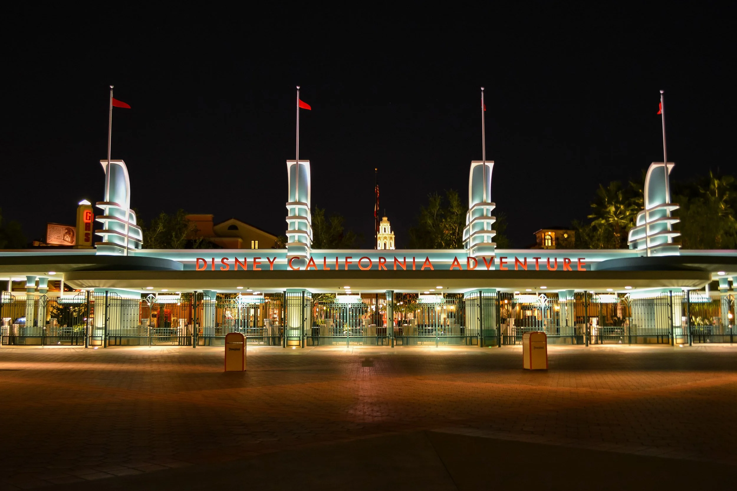 Adventure Awaits - A symmetrical night photograph showcasing the illuminated art deco entrance gates of Disney California Adventure park, featuring neon lettering and stylized architectural pylons under a dark sky.