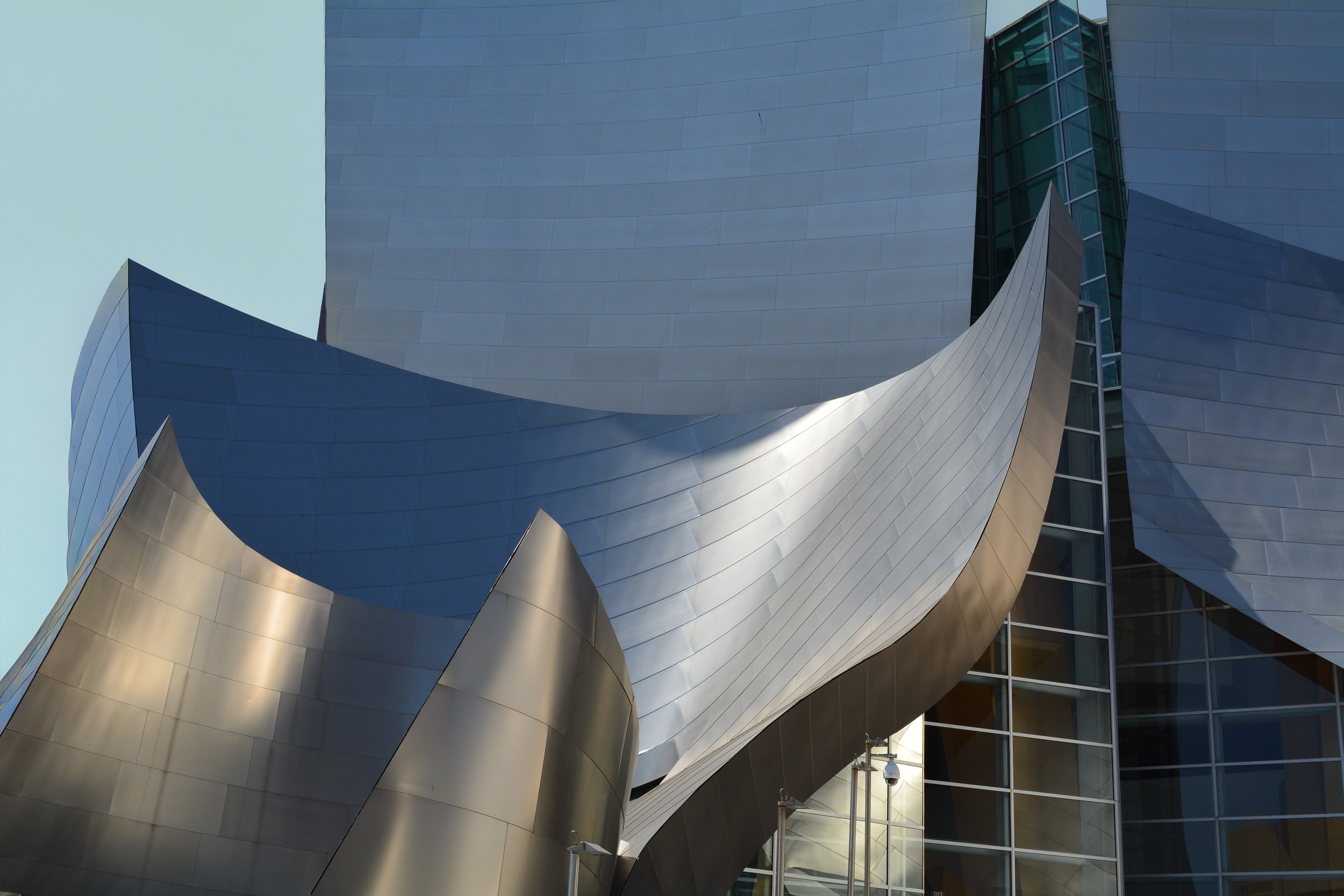 Symphonic Curves - A detailed architectural study capturing the sweeping, metallic titanium sails of the Walt Disney Concert Hall, highlighting the dramatic play of bright afternoon sunlight and soft shadows reflecting off the curved surfaces.