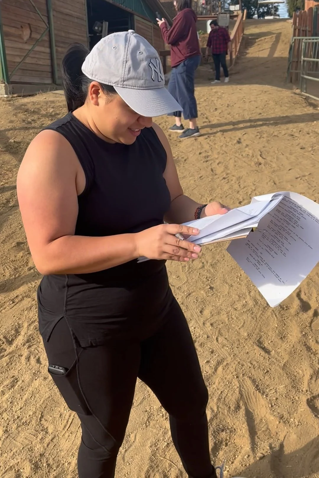 Behind-the-scenes portrait of screenwriter Lauren Ernest smiling and reviewing a printed script on a sunny outdoor film set.