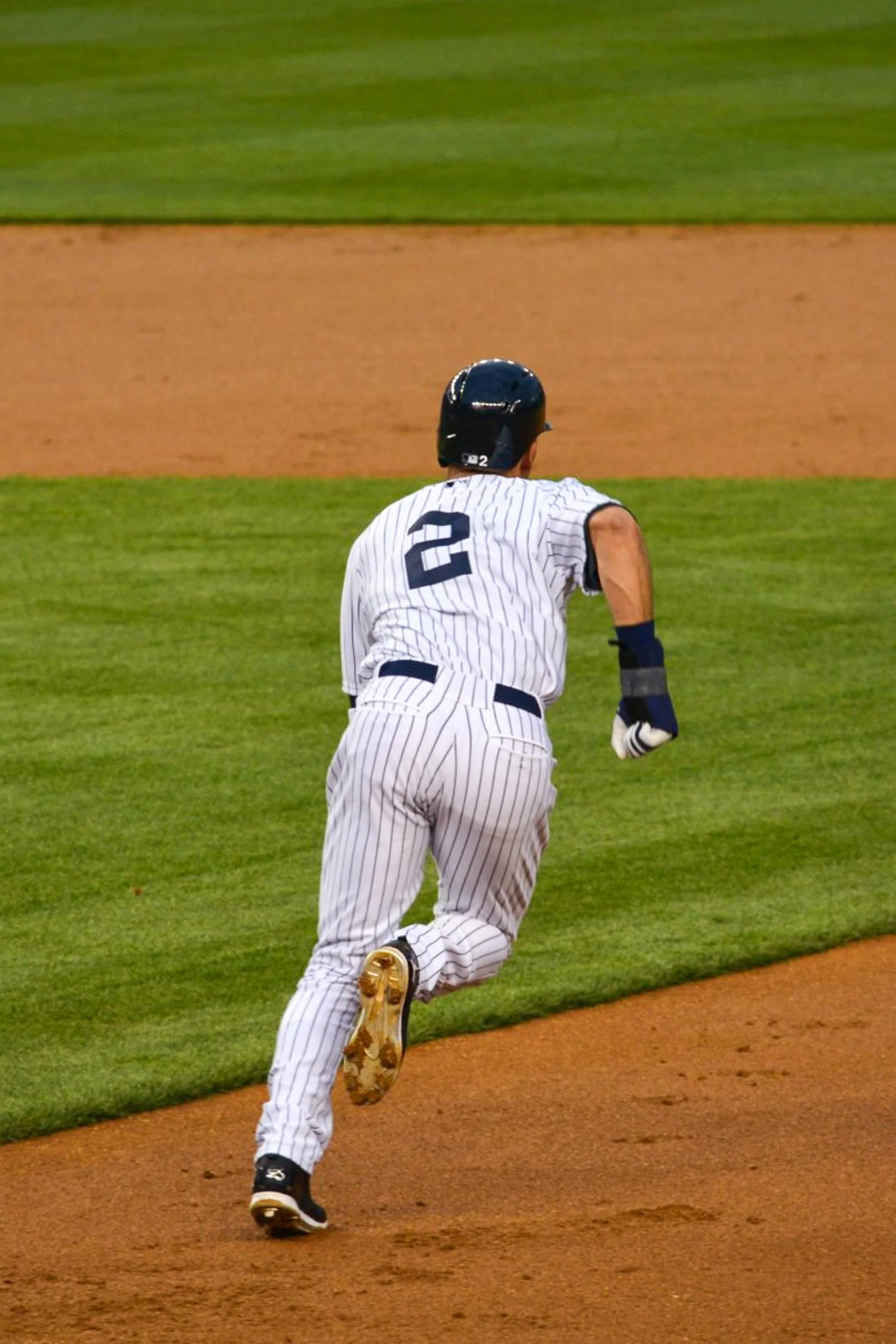 The Captain's Sprint - A dynamic, action-oriented vertical shot from behind Derek Jeter wearing his iconic number 2 pinstripes, sprinting hard across the diamond between the green outfield grass and the dirt base path.
