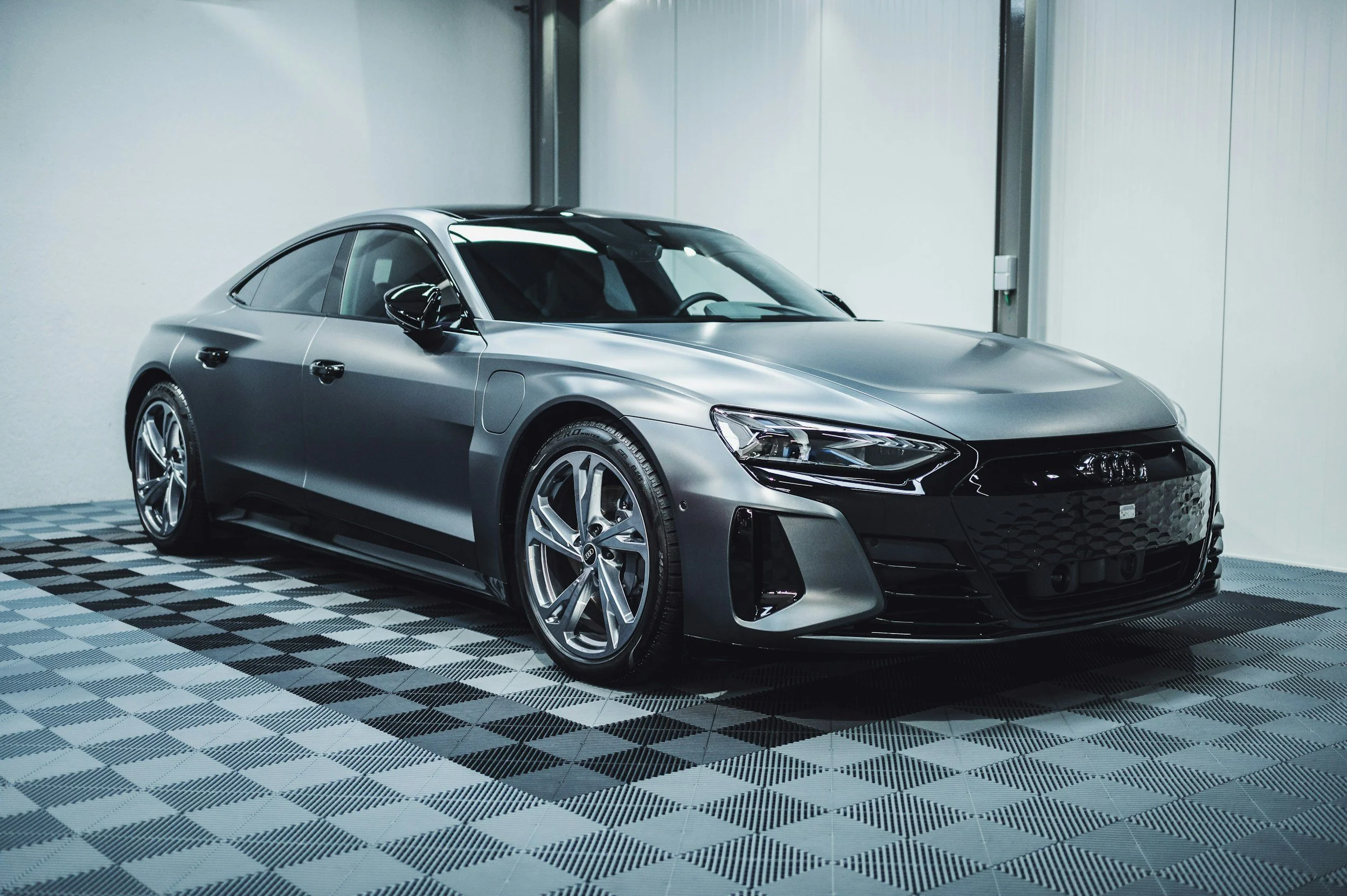 A sleek, silver Audi sedan parked indoors on a patterned floor against a plain wall.