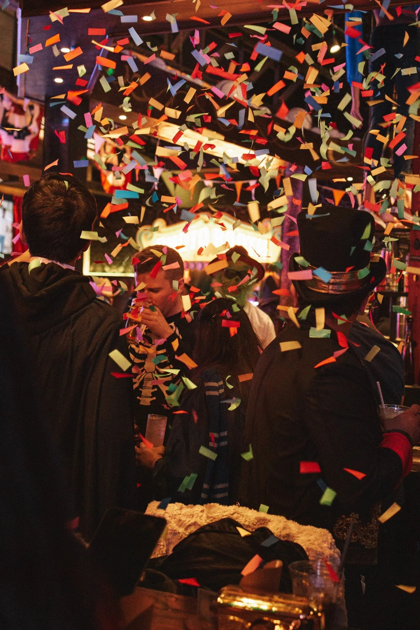 People celebrating with falling colorful confetti in a lively indoor setting, possibly a party or event.
