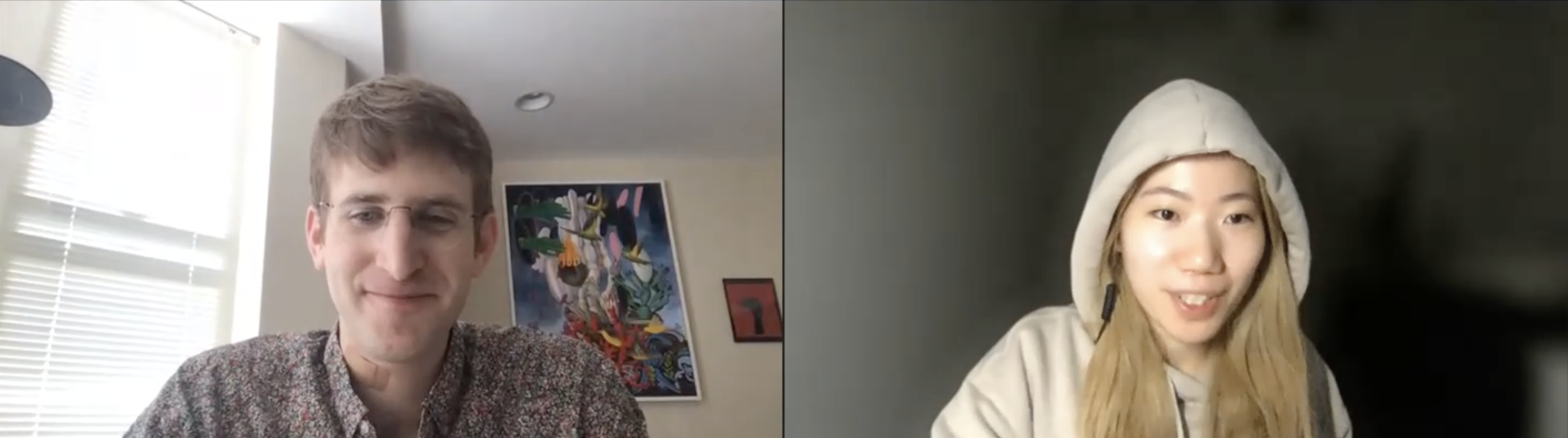A man with glasses and a woman with long blonde hair wearing a hoodie participate in a video call. The man is in a well-lit room with colorful artwork on the wall behind him. The woman is in a dark room with a hood over her head, smiling at the camera.