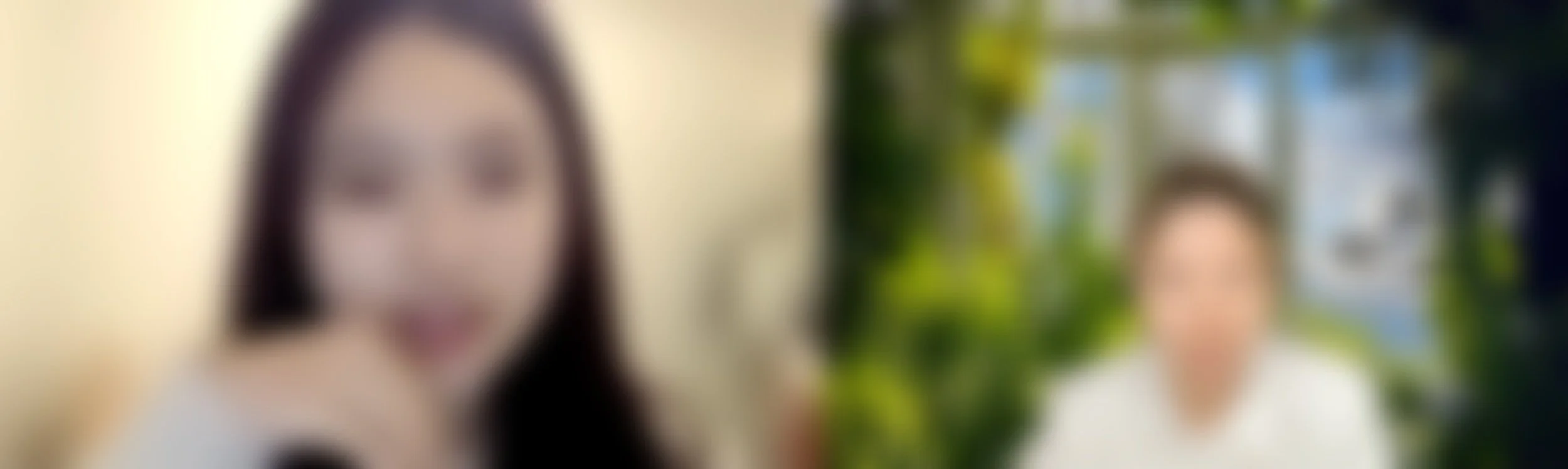 Blurred image of two women, one with dark hair and one with lighter hair, standing outdoors surrounded by greenery.