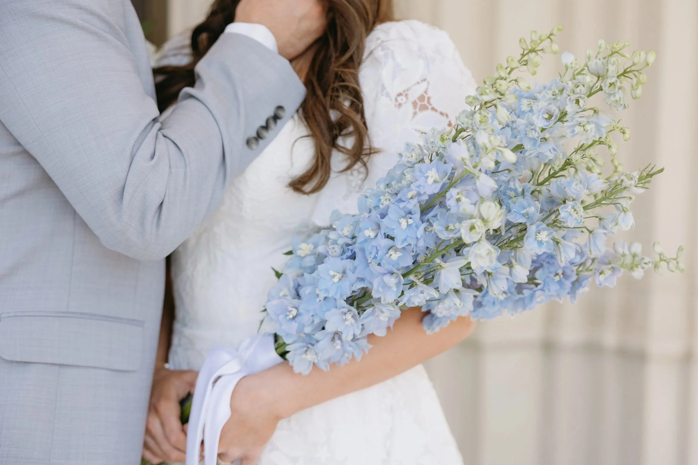 A bride holding a large bouquet of light blue delphinium flowers during a wedding ceremony.