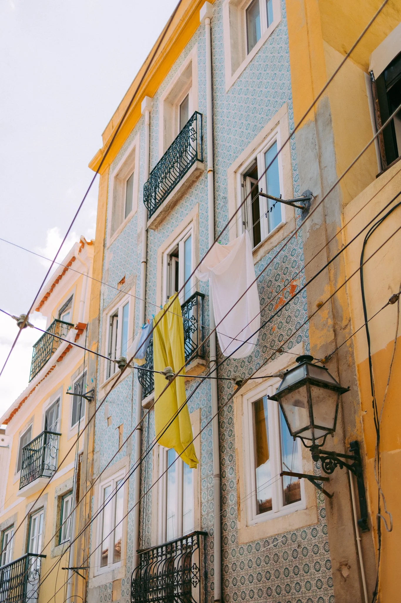 Apartment building with colorful tiled facade, small balconies with black iron railings, laundry hanging on clotheslines, and a wall-mounted lantern.