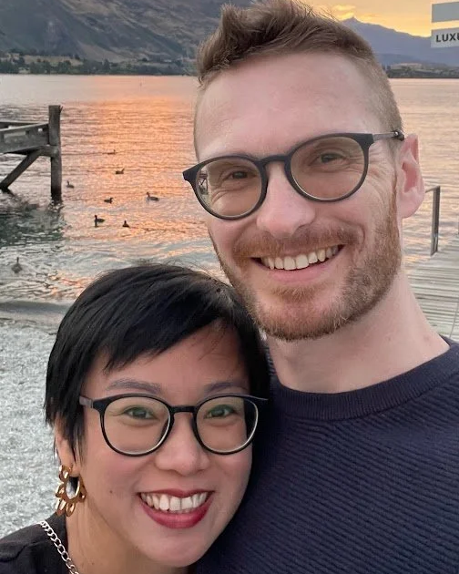 Photo of Pastor Geoff Vucetich and his wife smiling in front of Lake Wanaka at sunset