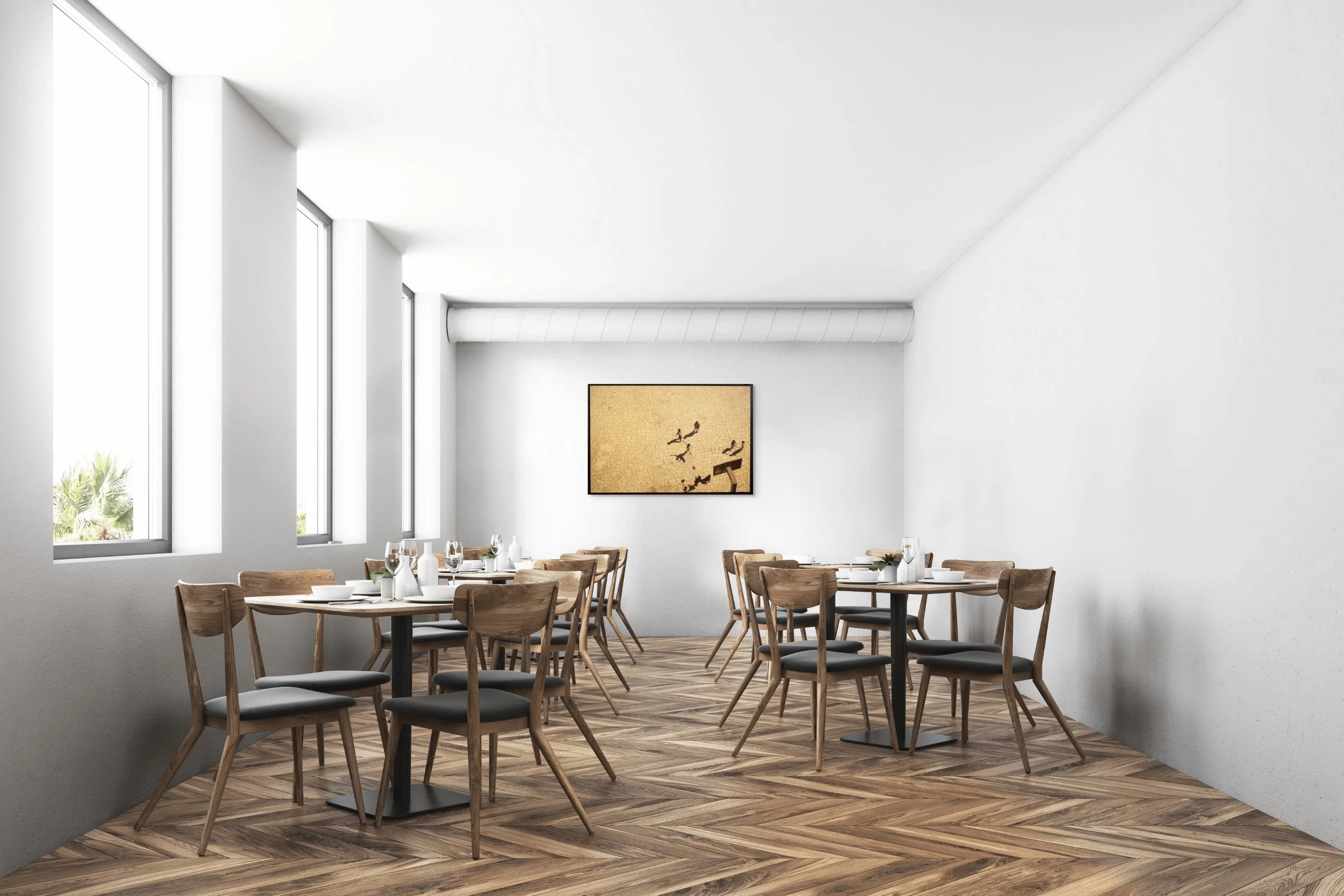 Restaurant dining area with wooden tables set with white dishes, glasses, and utensils, and wooden chairs, illuminated by large windows, with a beige abstract art piece on the white wall.