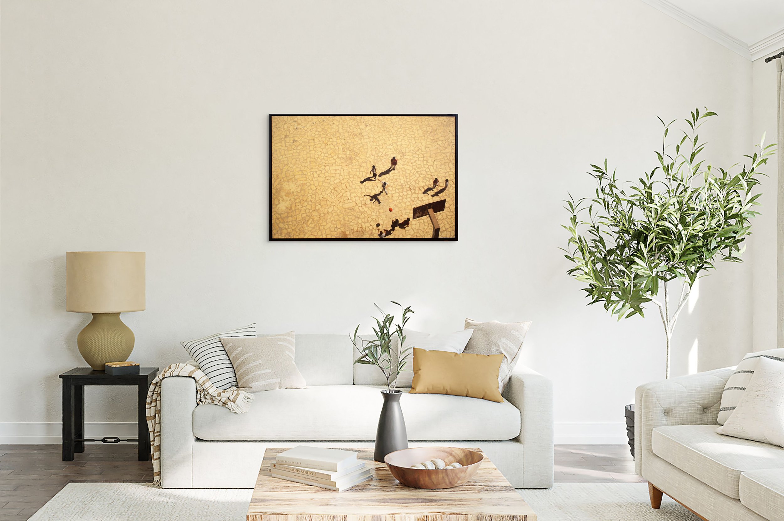 Bright and airy living room with a white sofa, beige pillows, a tall green plant, a wooden coffee table with a bowl and books, a side table with a beige lamp, and a framed artwork on the wall.