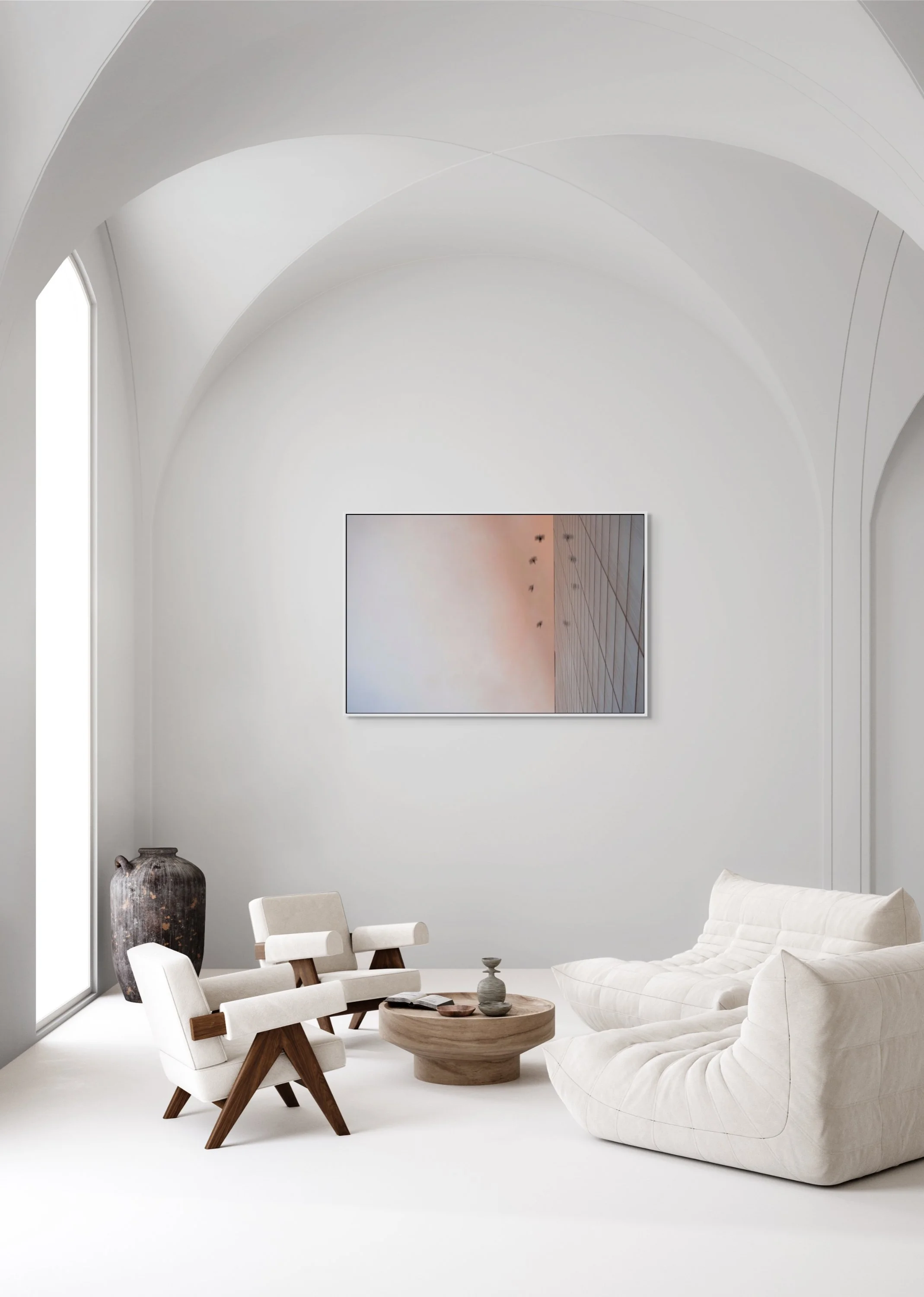 Minimalist living room with white walls and ceiling, large window, beige sofa, two armchairs with wooden legs, round wooden coffee table, large dark vase in corner, framed wall art with pastel tones