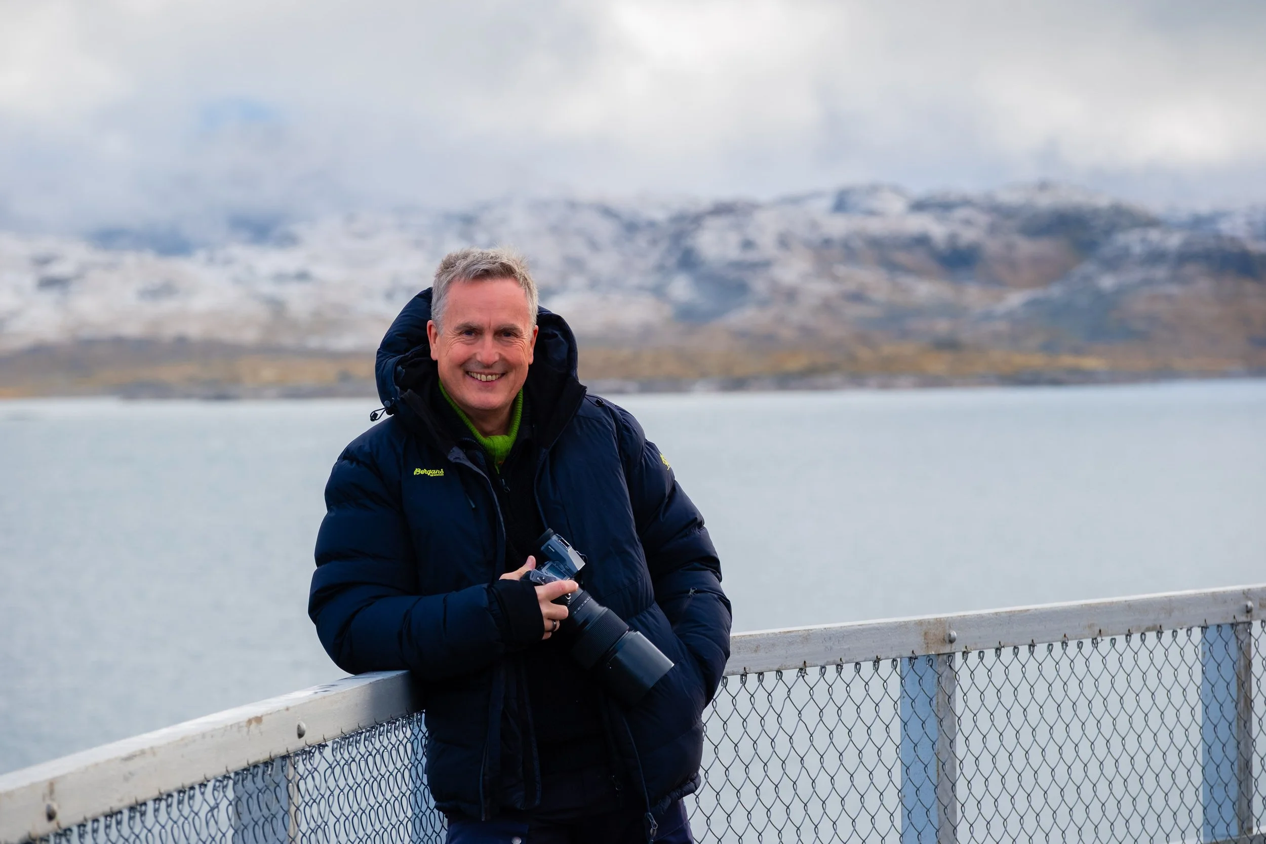 En mann står utendørs i snødekte fjell i Norge, med et kamera på stativ.