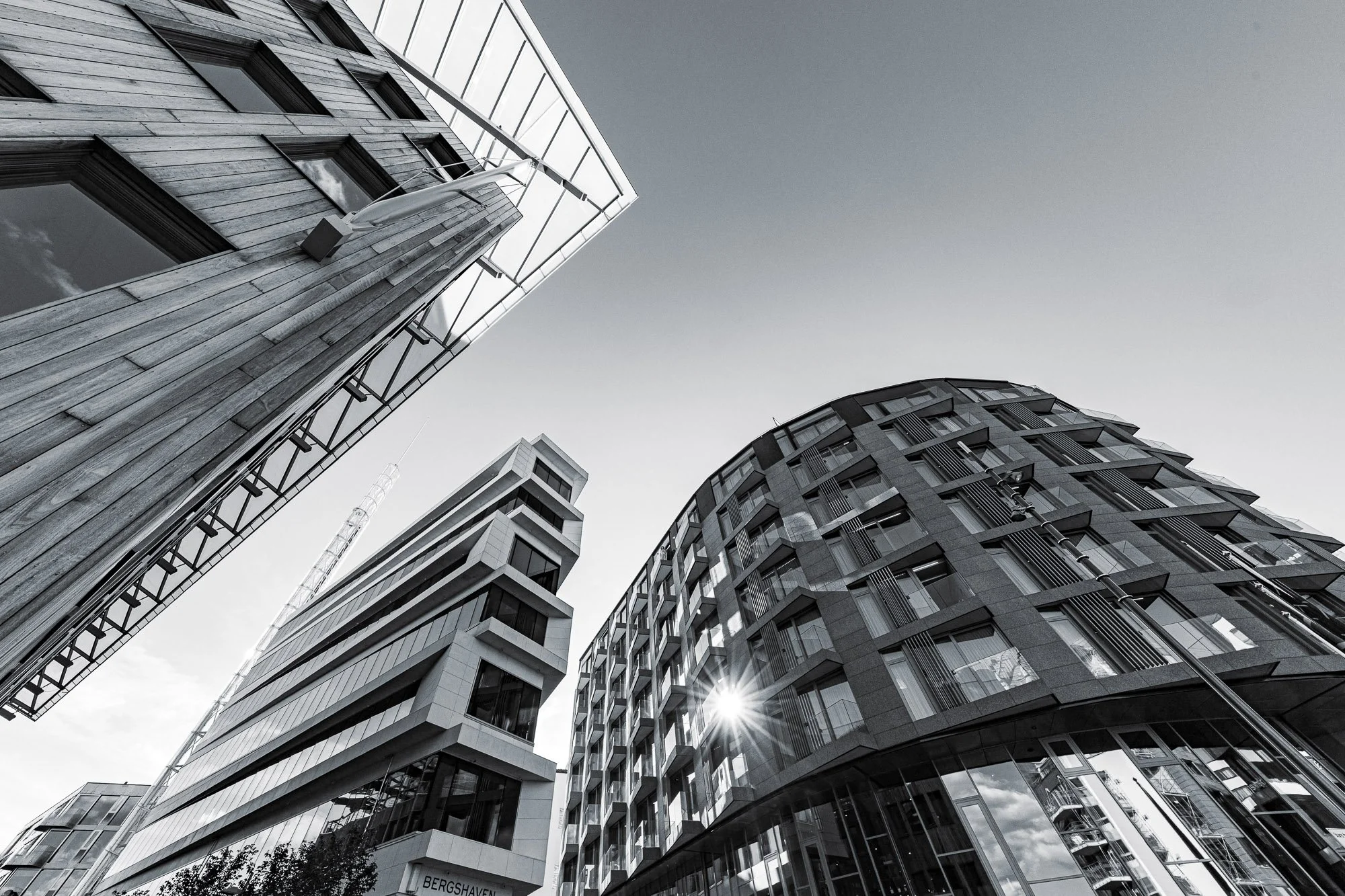 Bilde av moderne høyblokker sett fra bakken med en klar himmel og sol som skinner gjennom bygningene.