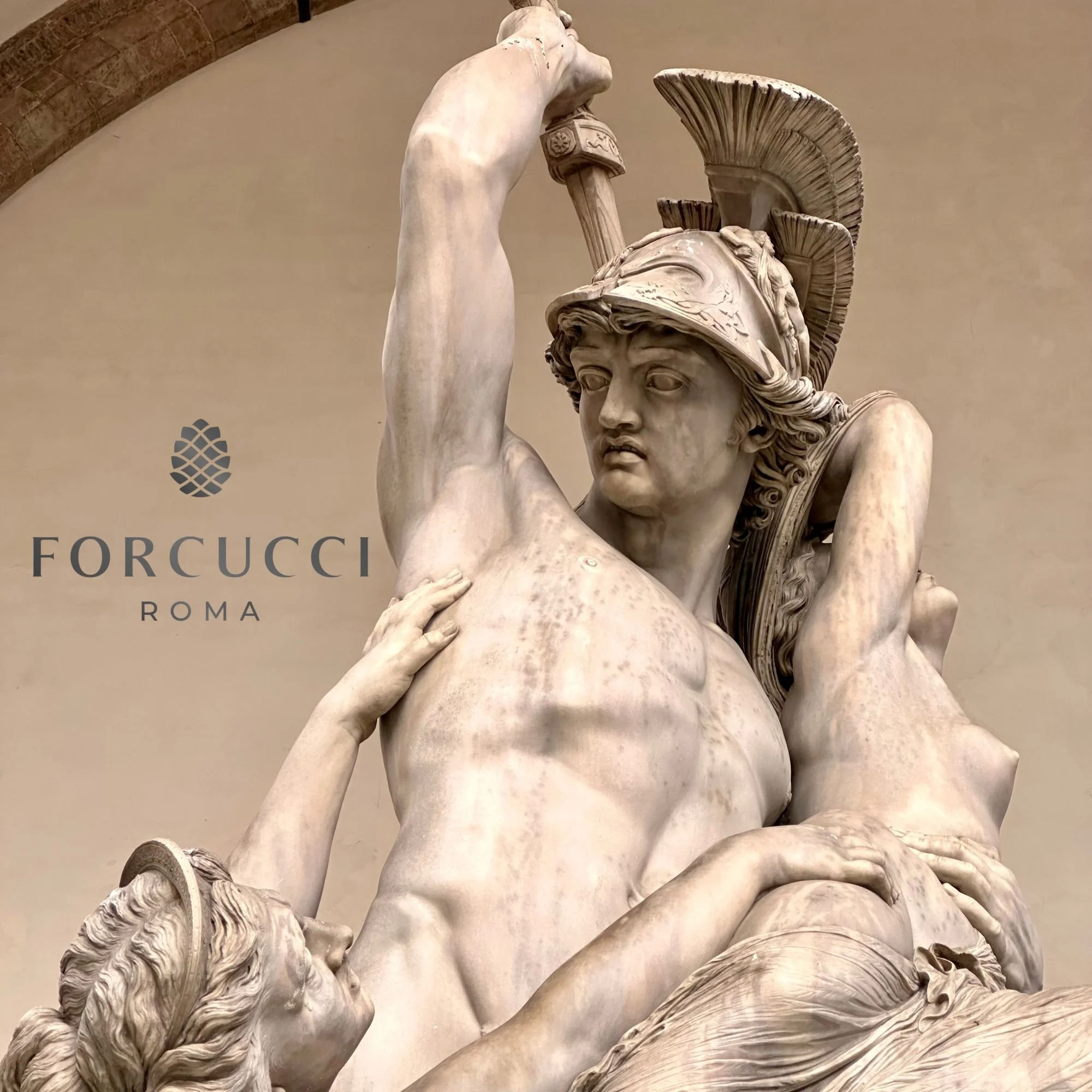 Marble sculpture of a warrior wearing a helmet with a crest, surrounded by reclining figures, in a museum setting with 'Forucci Roma' logo on the wall