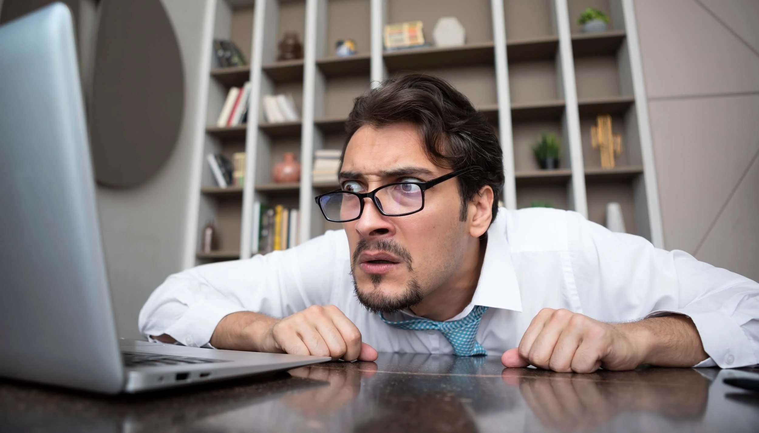 man with glasses looking confused at laptop