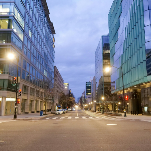 Empty city street lined with modern office buildings at dusk with streetlights on