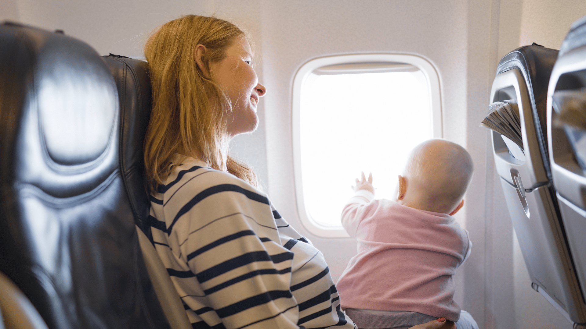 A nanny holding a baby on her knee on a plane