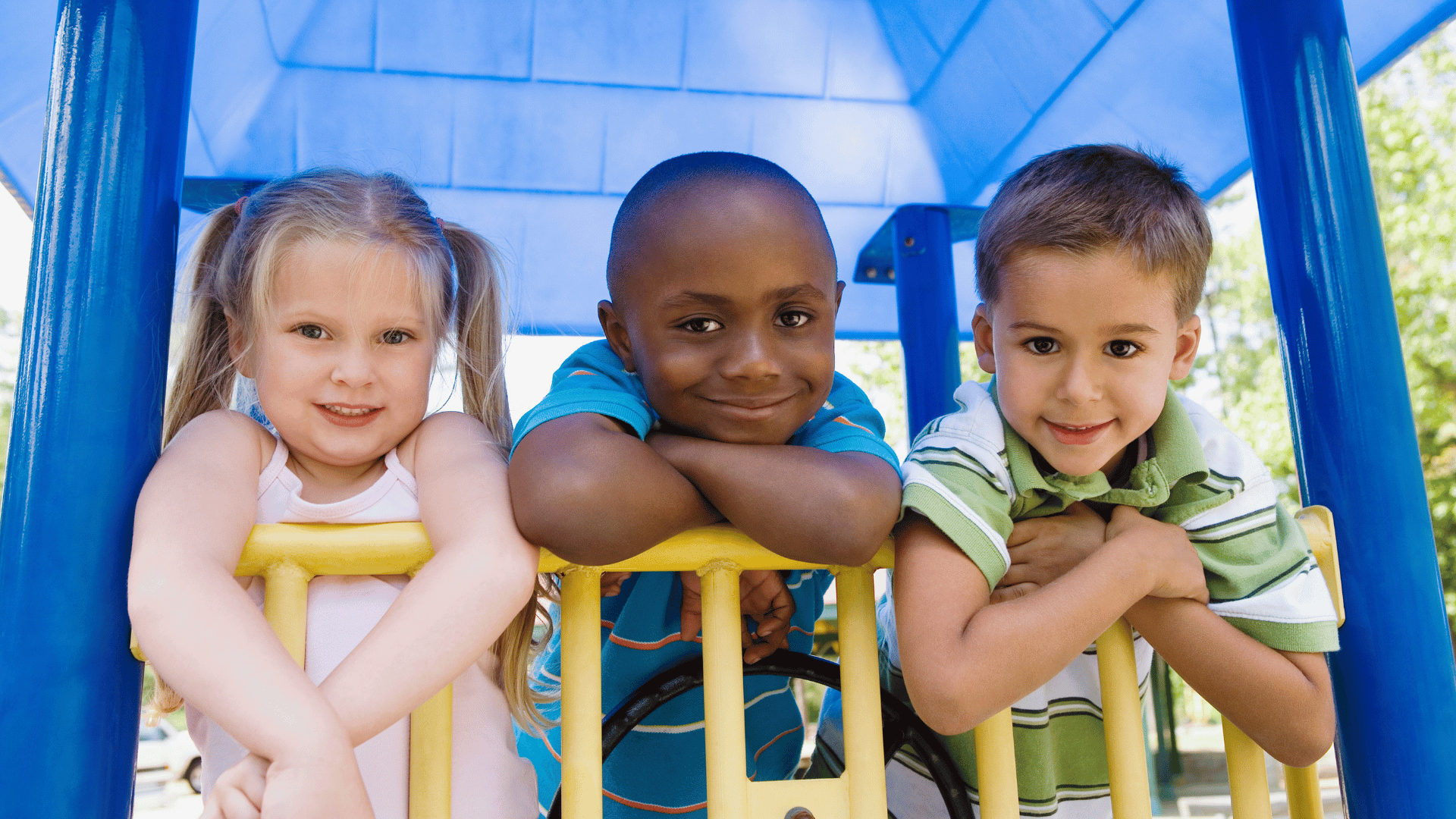 Three children leaning over railings in a playhouse at a playground