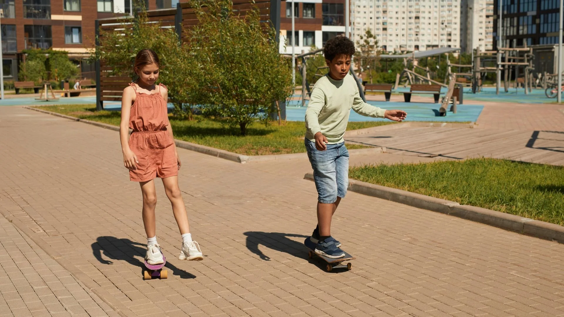 Two children riding skateboards through a pedestrianized neighborhood