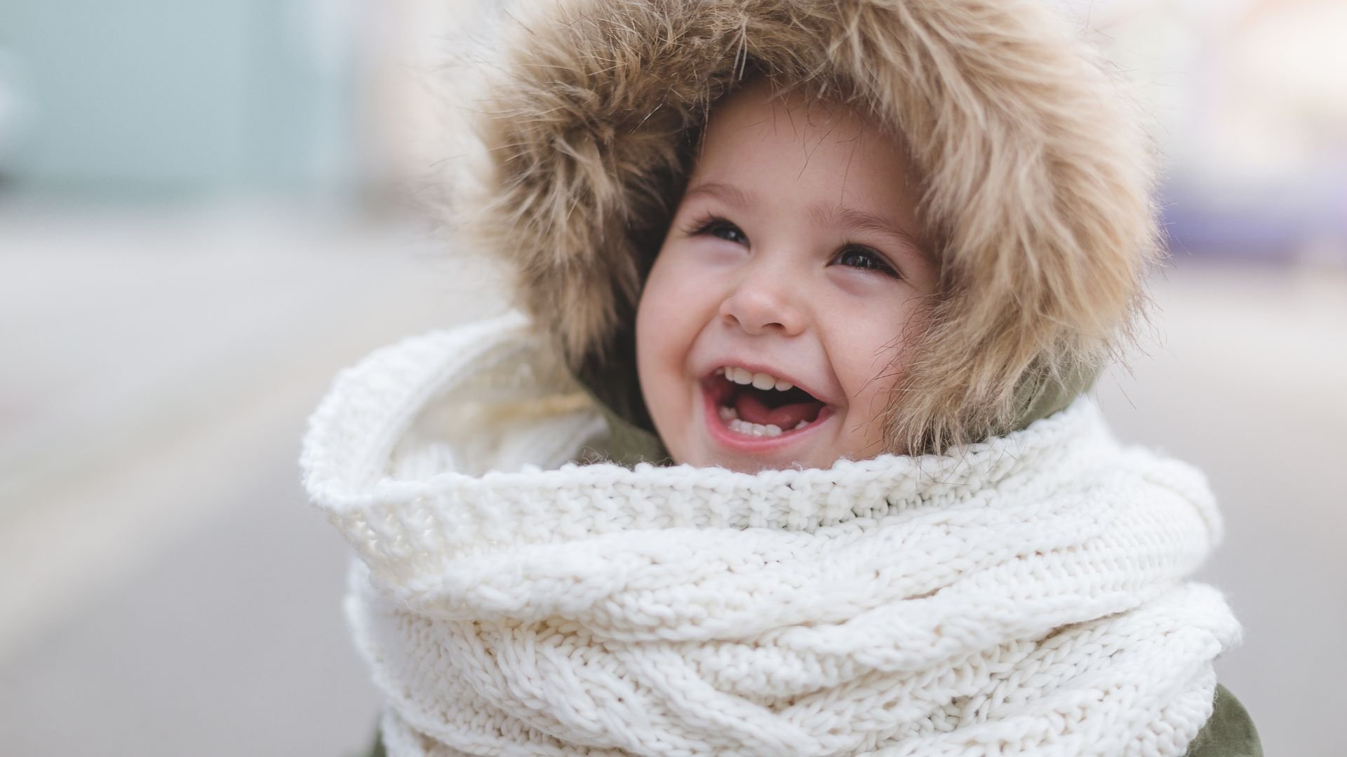 A laughing toddler wrapped up in winter clothes