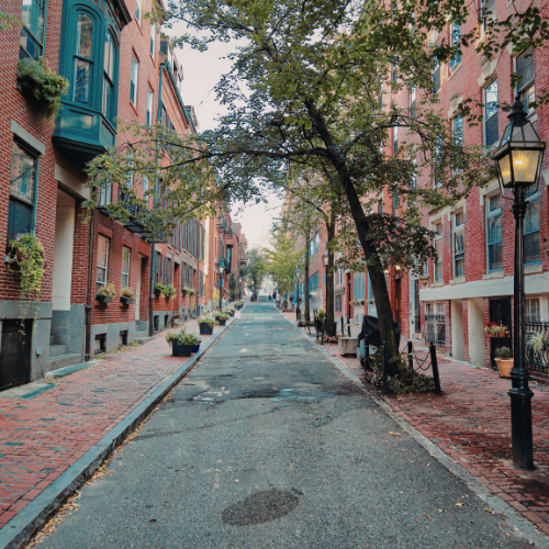 Quiet cobblestone street lined with brick townhouses and trees in a historic neighborhood