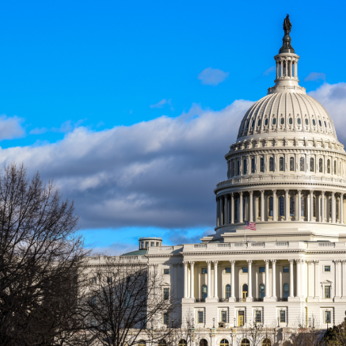 United States Capitol building under a blue sky with clouds and trees in the foreground