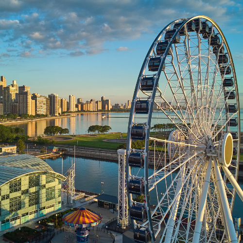 Large Ferris wheel by the waterfront with a city skyline and high-rise buildings in the background under a partly cloudy sky.