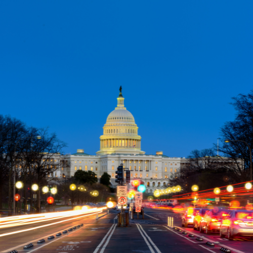 U.S. Capitol building illuminated at dusk with traffic light trails on the street leading toward it