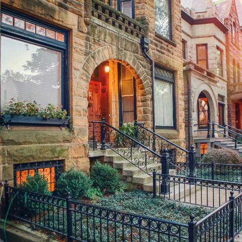 Historic stone townhouse entrance with arched doorway, wrought-iron railings, and warm interior lighting on a residential street.