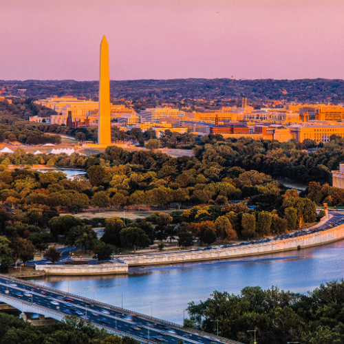 Washington Monument rising above the National Mall with the Potomac River and surrounding cityscape at sunset