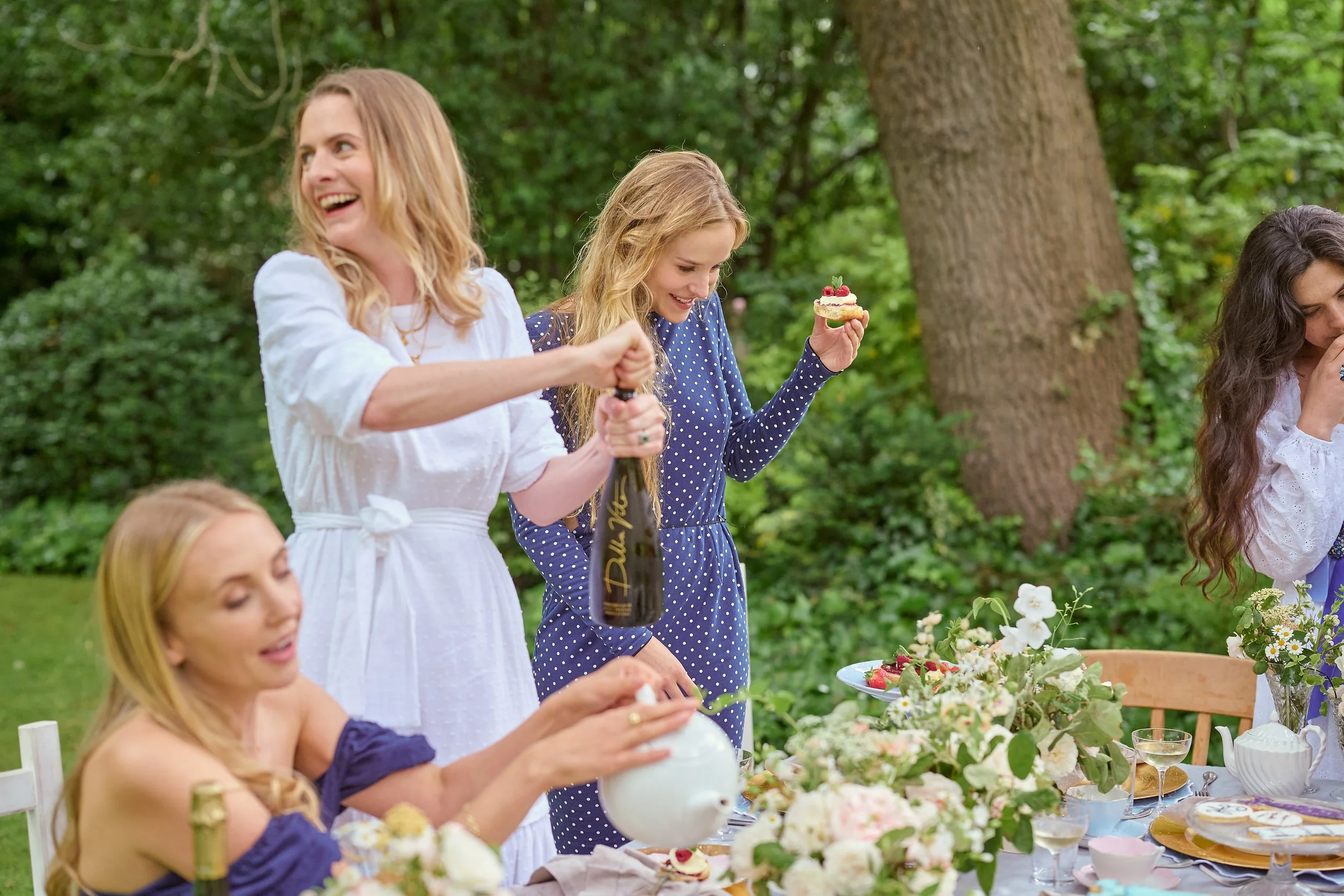 Women celebrating at an outdoor garden party with a decorated table, flowers, and desserts.
