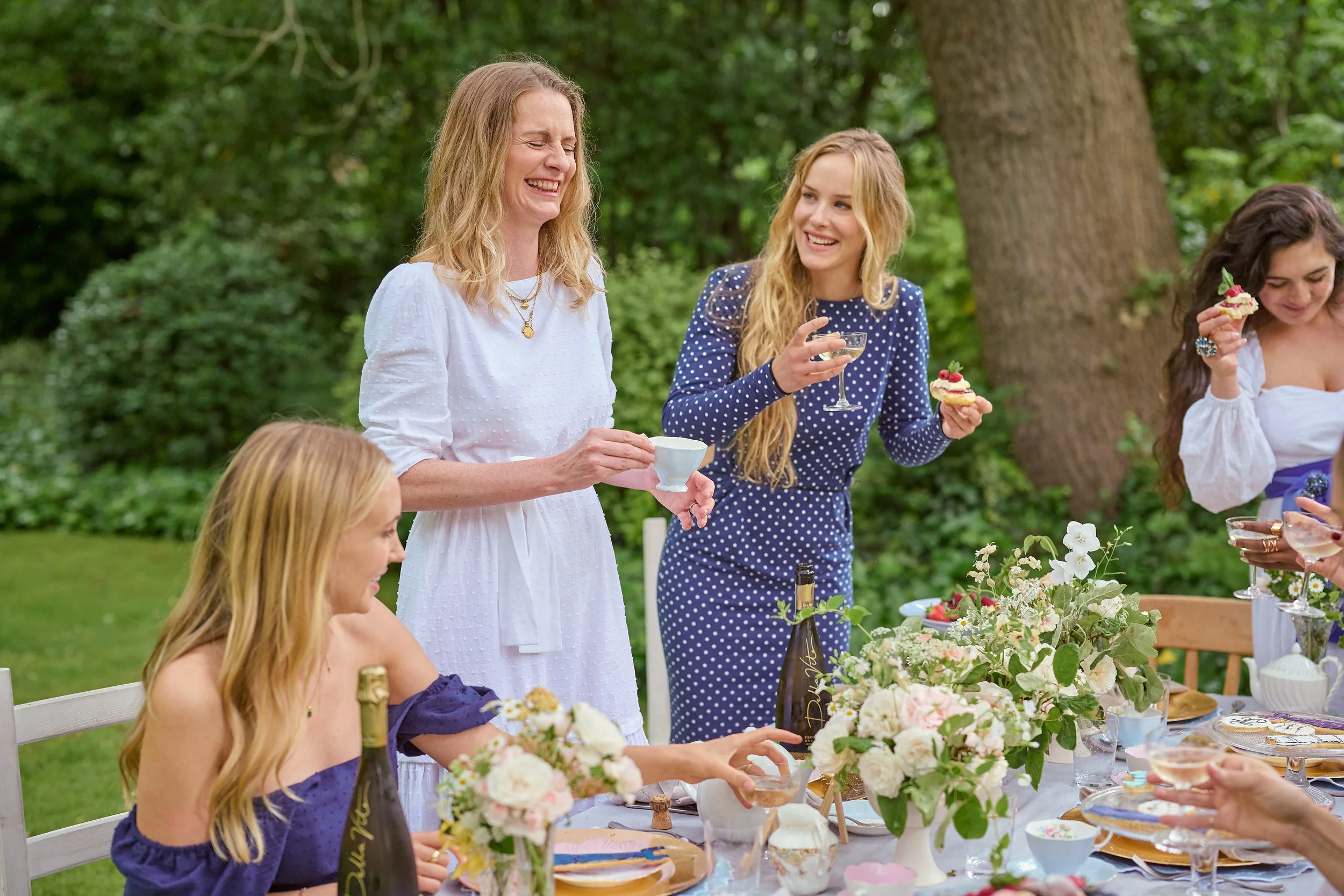 A group of women enjoying a garden party with food and drinks, decorated with flowers.