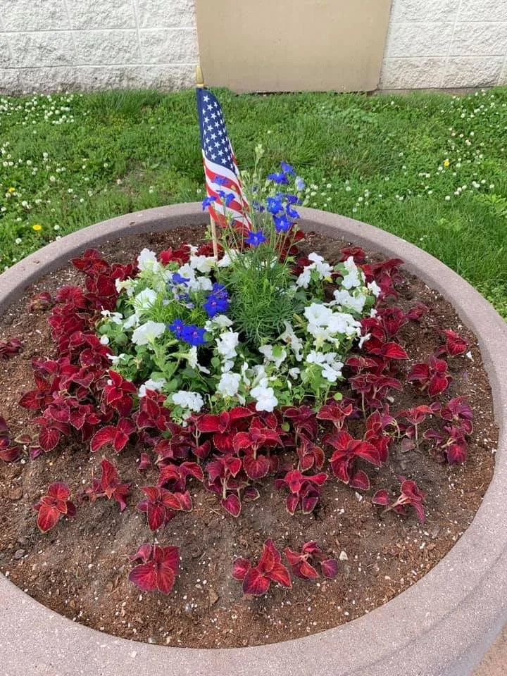 A pot with red folliage, white and blue flowers, and a small American flag in the center