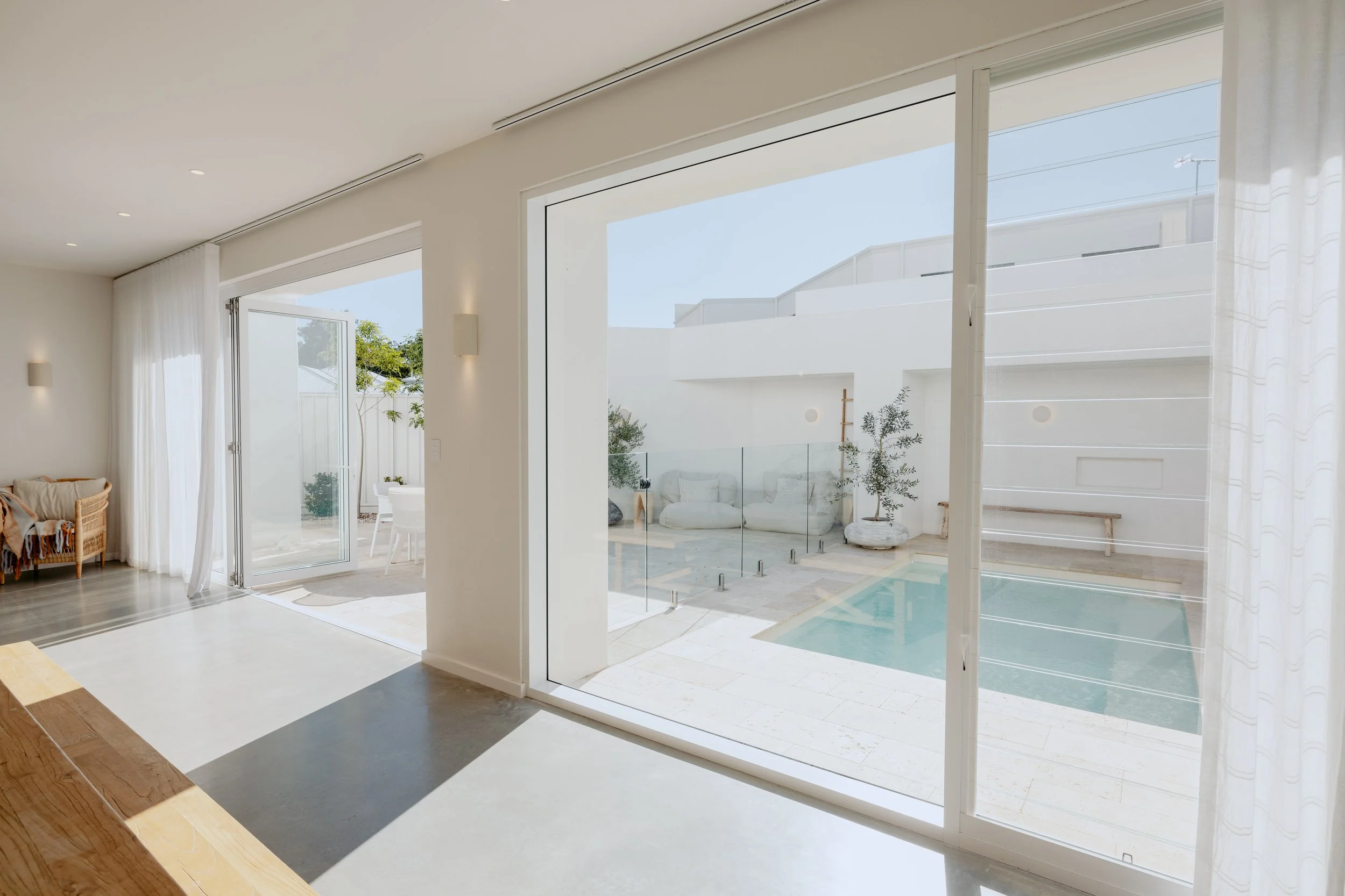 Interior view of a modern home with large glass sliding doors leading to a small outdoor patio with lounge chairs, a small pool, and potted plants.