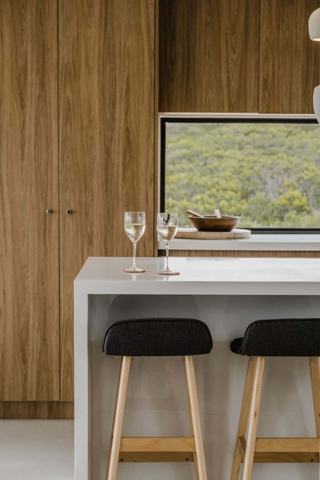 Two glasses of sparkling water on a white kitchen island with black bar stools and a window showing green trees outside.